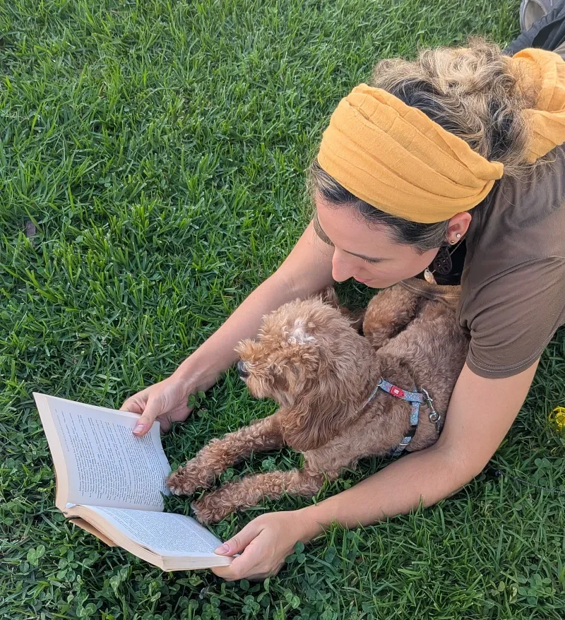 Ruthie Ayzenberg reading outdoors with her dog.