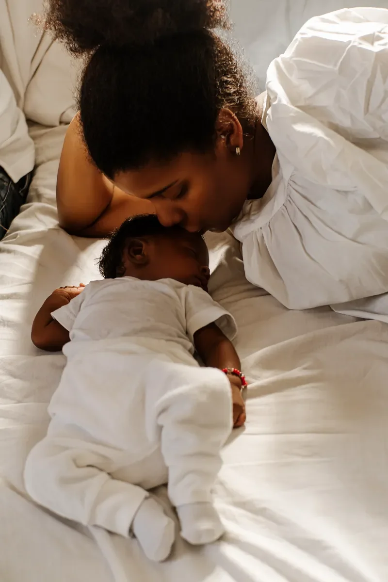 Mother resting beside her newborn baby in bed.