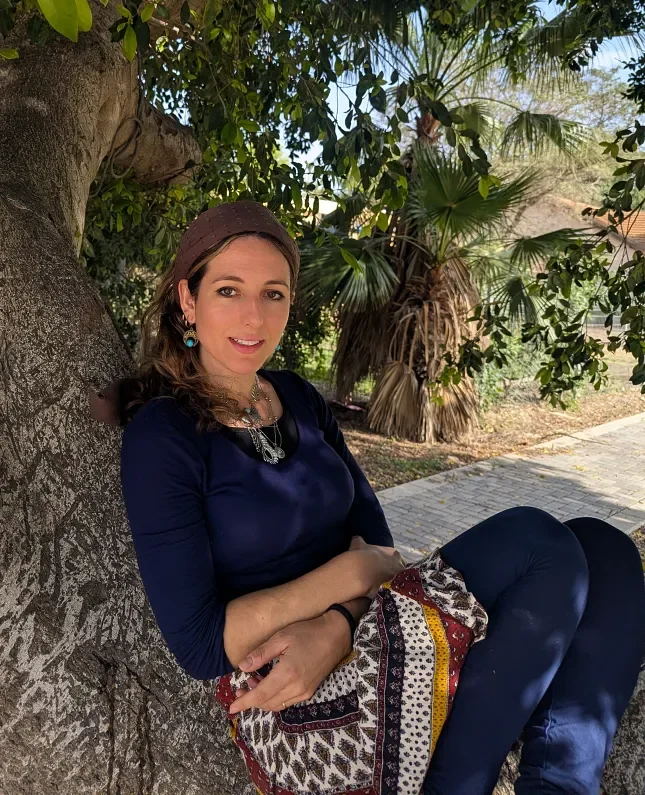 Ruthie Ayzenberg seated outdoors beside a tree.