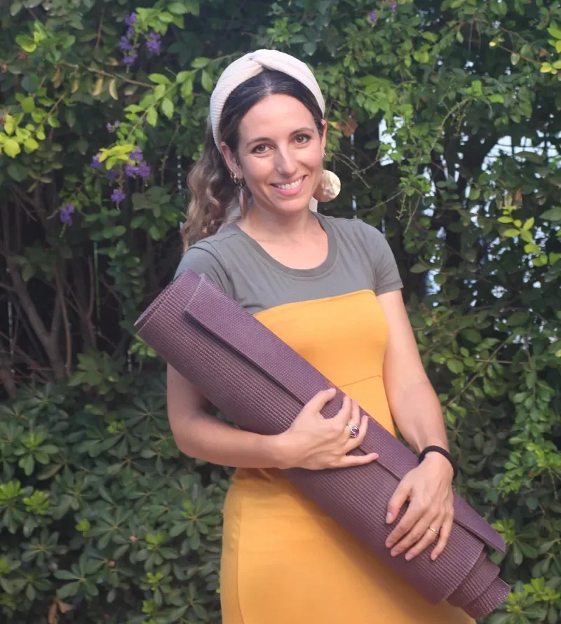 Ruthie Ayzenberg holding a yoga mat outdoors.