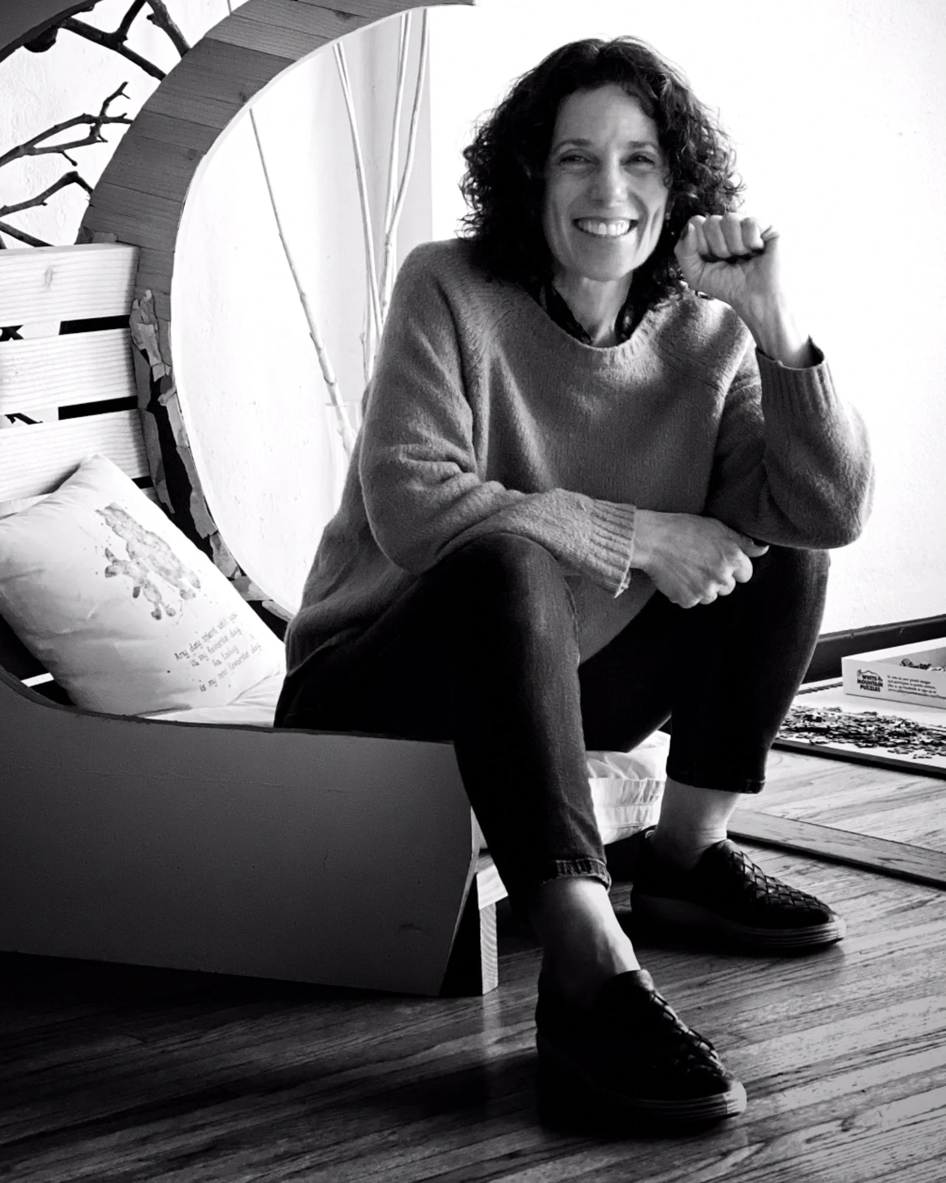 Black and white portrait of a smiling woman with curly hair, wearing a dark top and a delicate necklace.