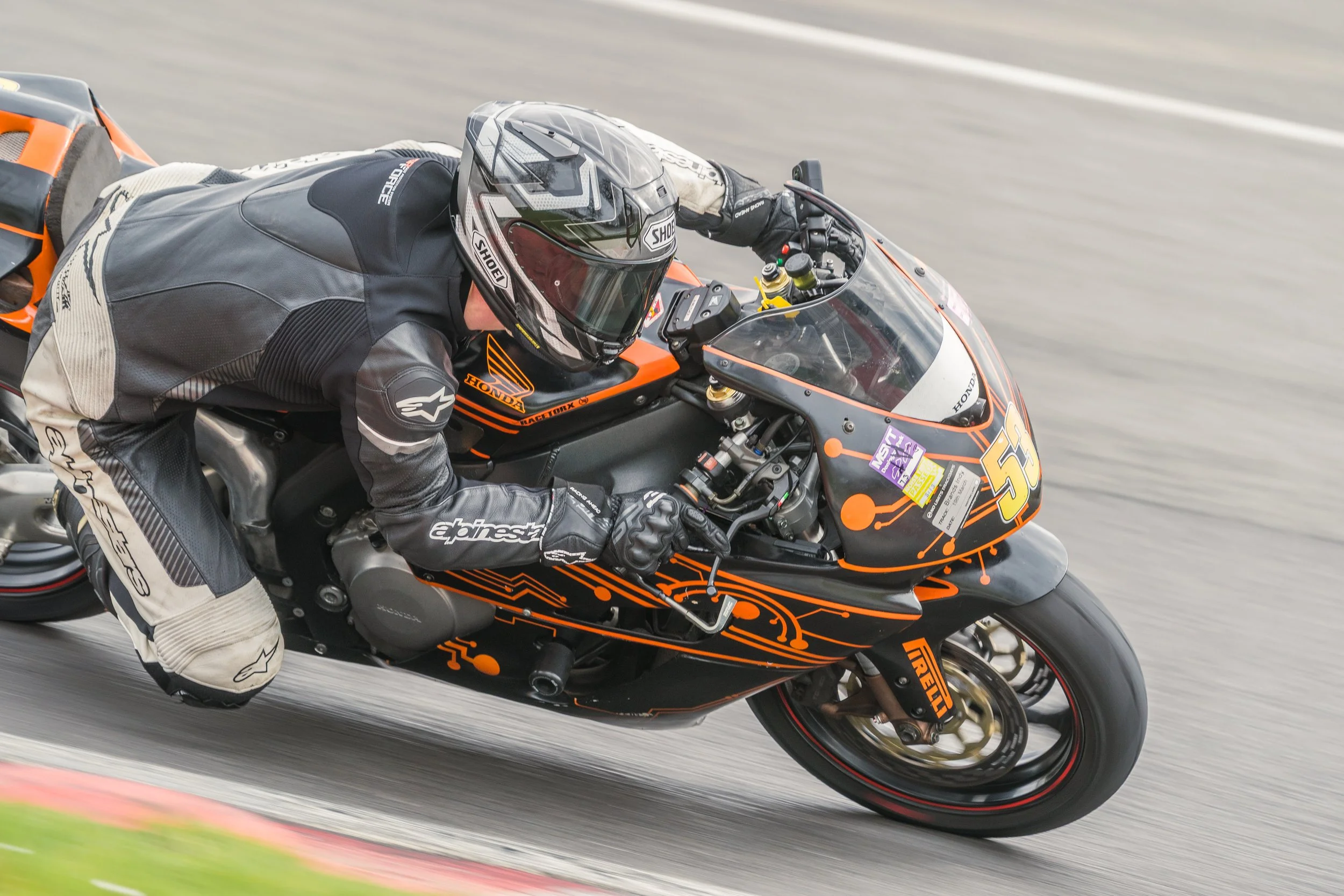 A motorcycle racer in full gear leaning into a turn on a black and orange racing motorcycle on a track.