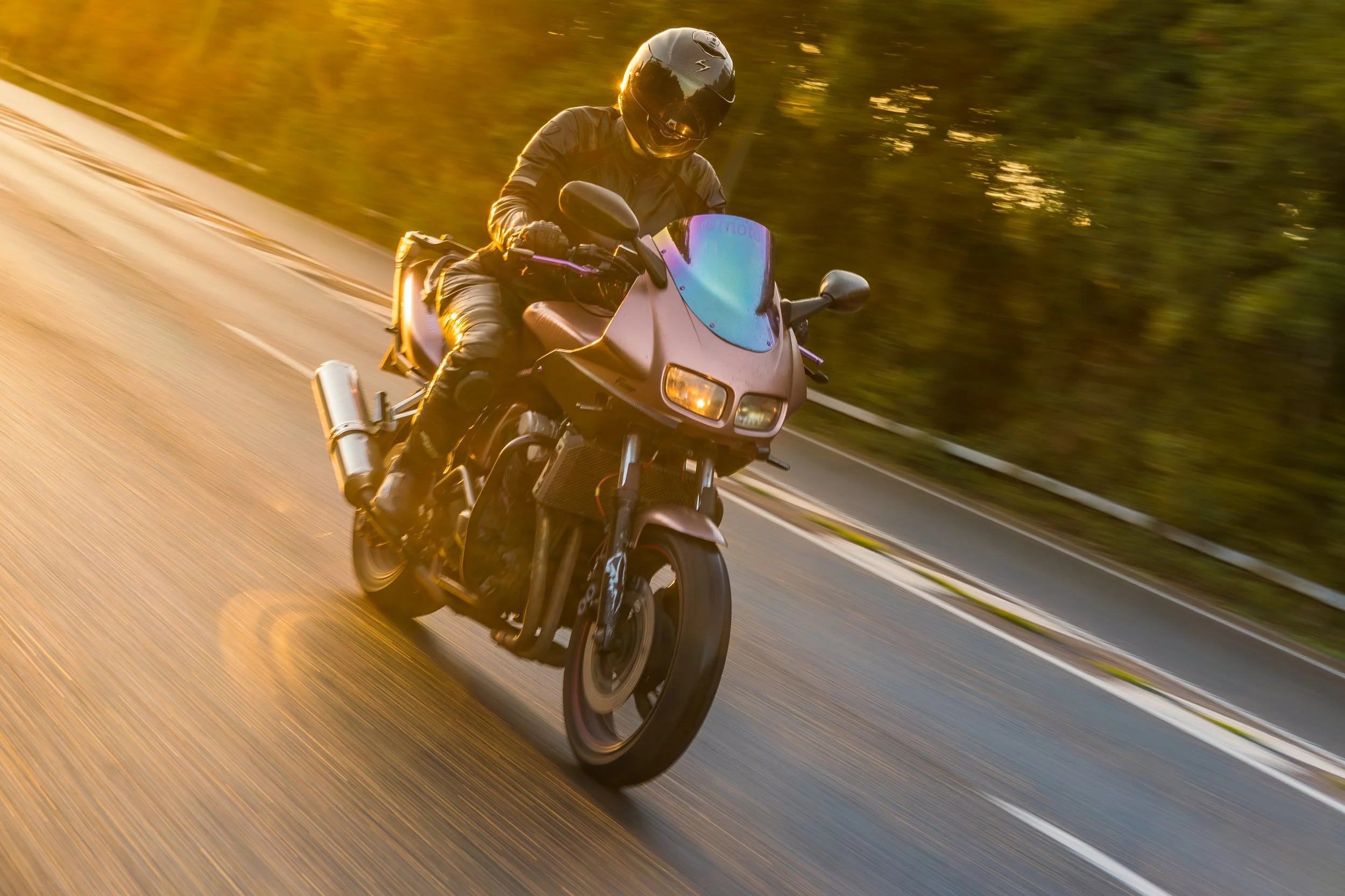 Motorcyclist wearing black helmet and gear riding on a highway during sunset.