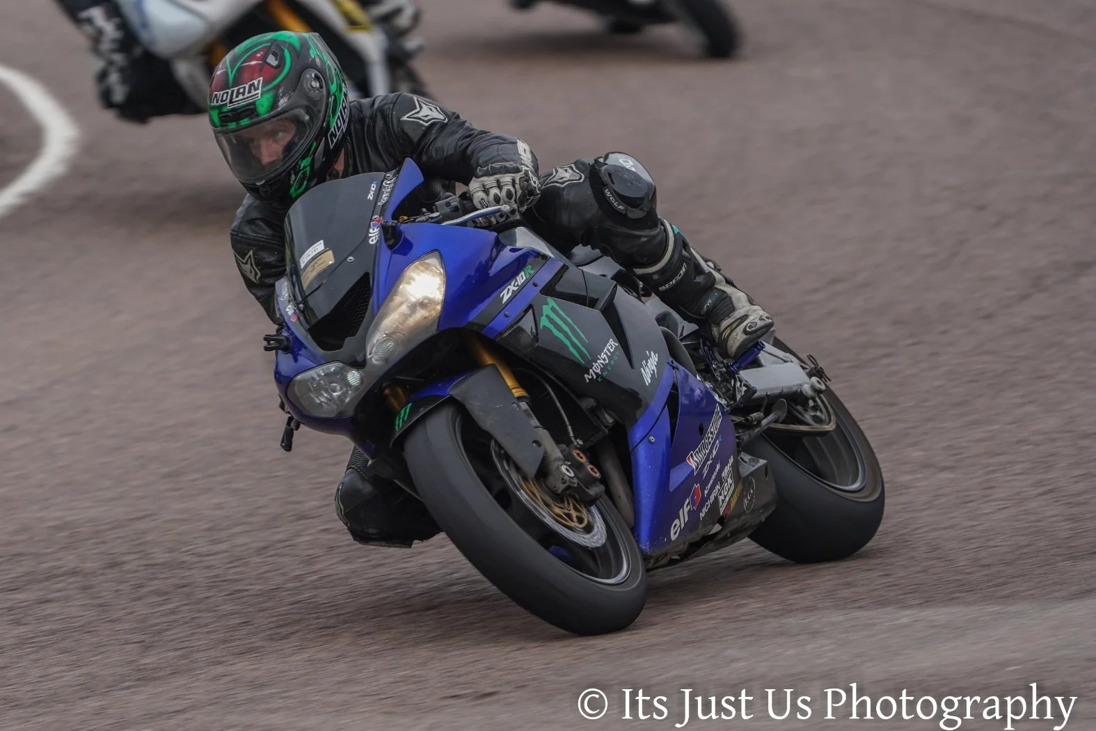 Motorcycle racer wearing a helmet and racing gear leaning into a turn on a blue Yamaha motorcycle on a dirt track.