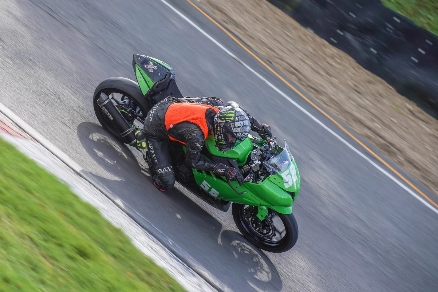 Motorcycle rider in black riding gear and helmet, riding a green sportbike on a racetrack.