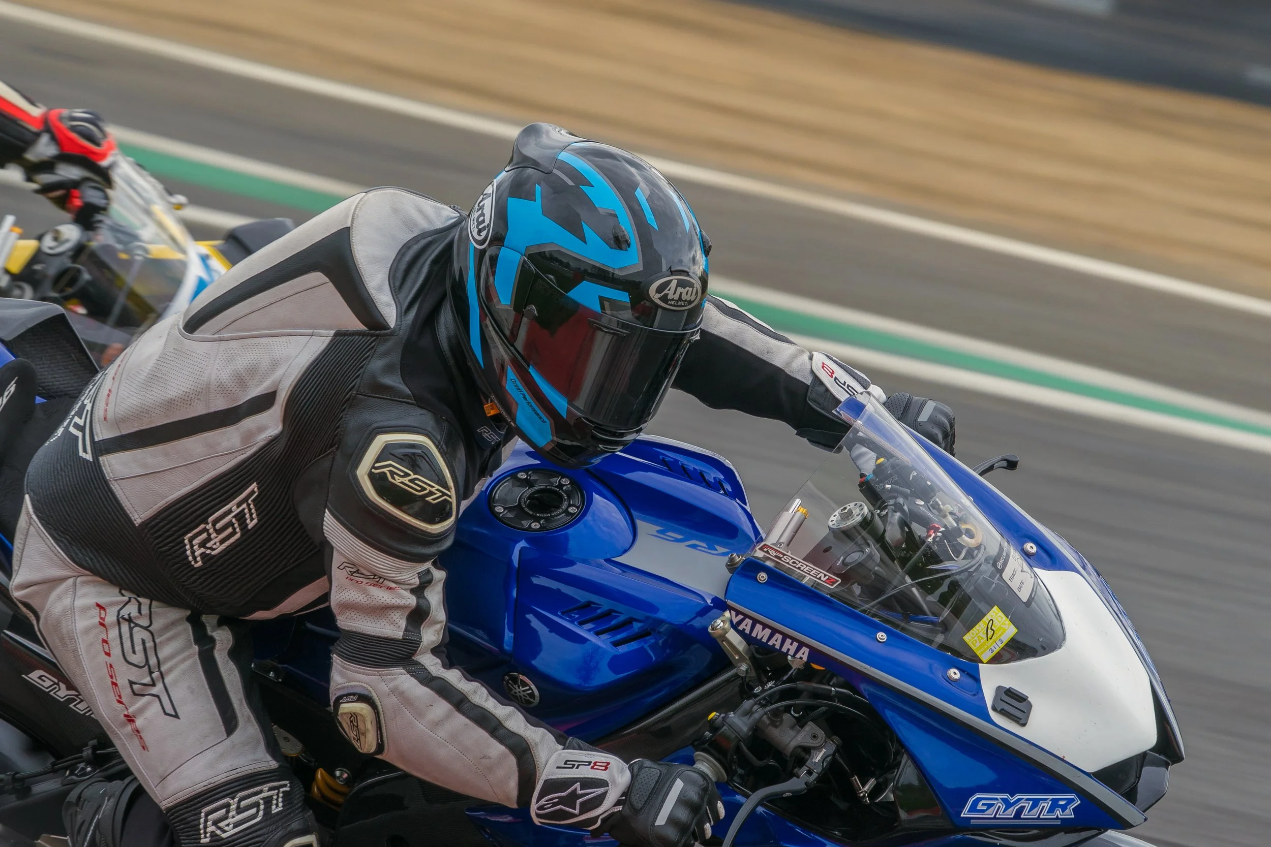 Motorcycle racer in racing suit and helmet riding a blue Yamaha sportbike on a race track.