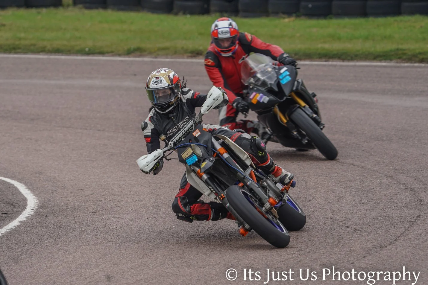 Two motorcycle racers leaning into a sharp turn on a racetrack, wearing full protective gear and helmets.