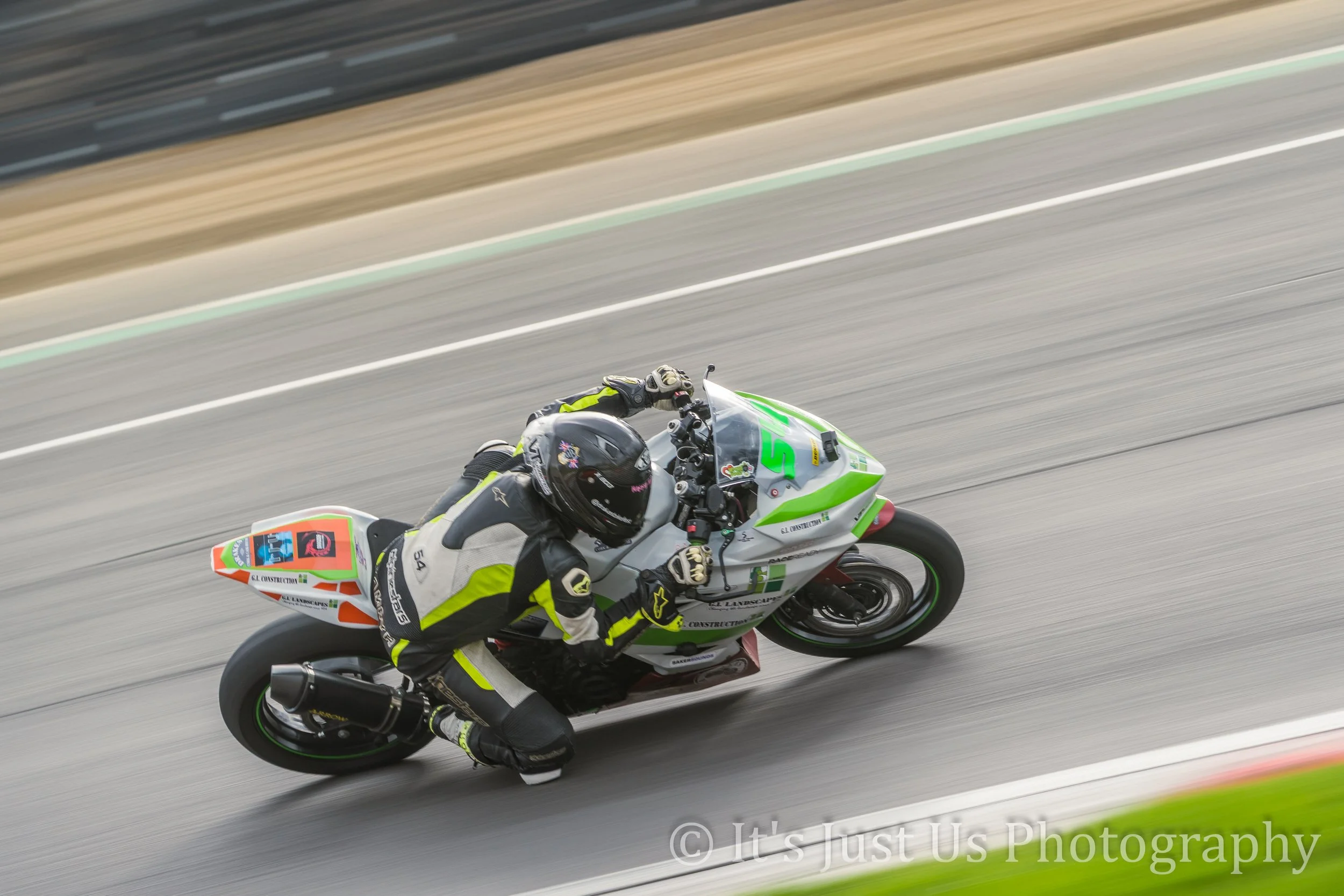 Motorcycle racer in black and fluorescent yellow gear leaning into a turn on a race track, with blurred background.