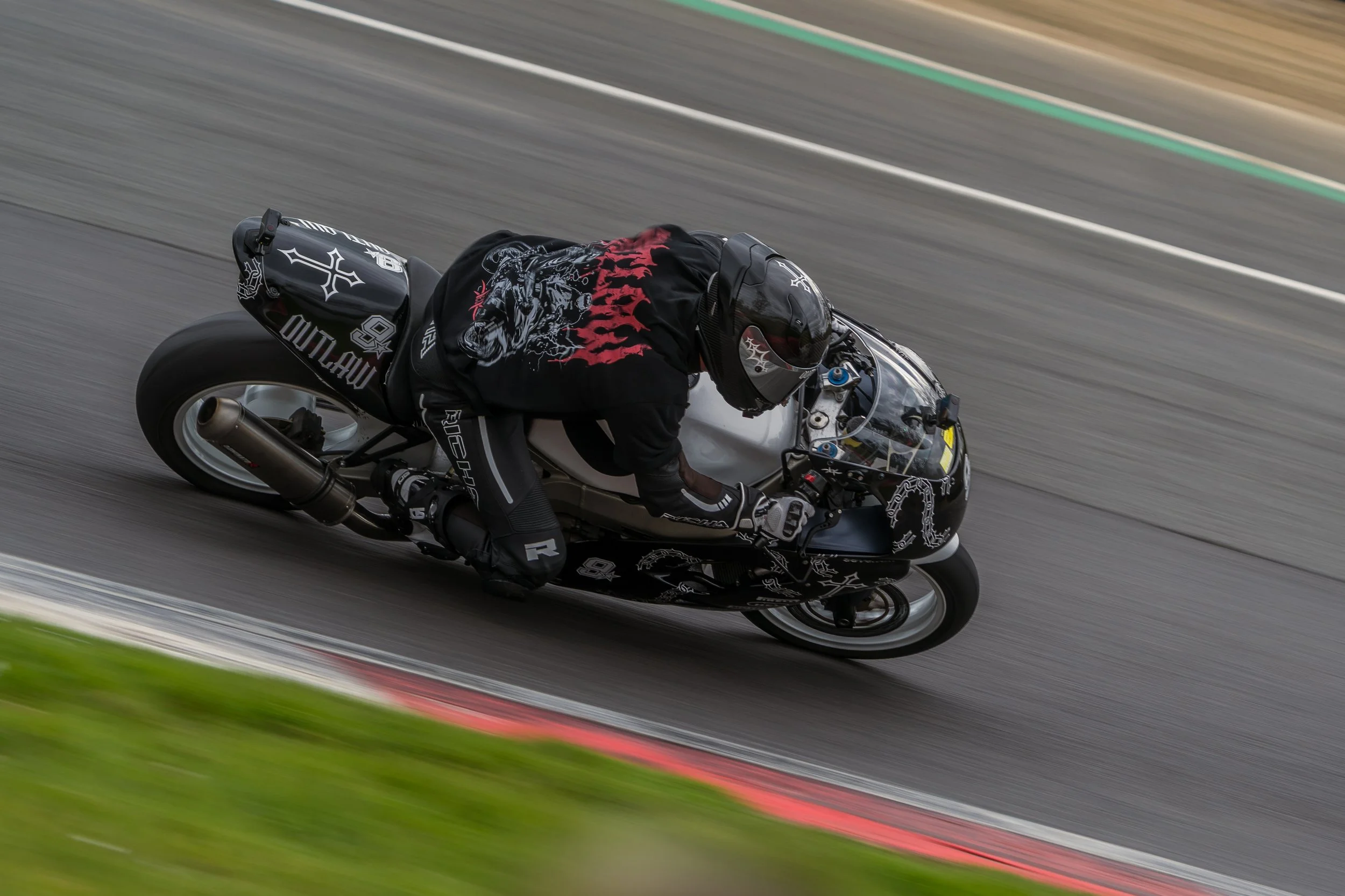 Motorcycle rider leaning into a turn on a racing track, wearing a black helmet and suit, on a black and white motorcycle.