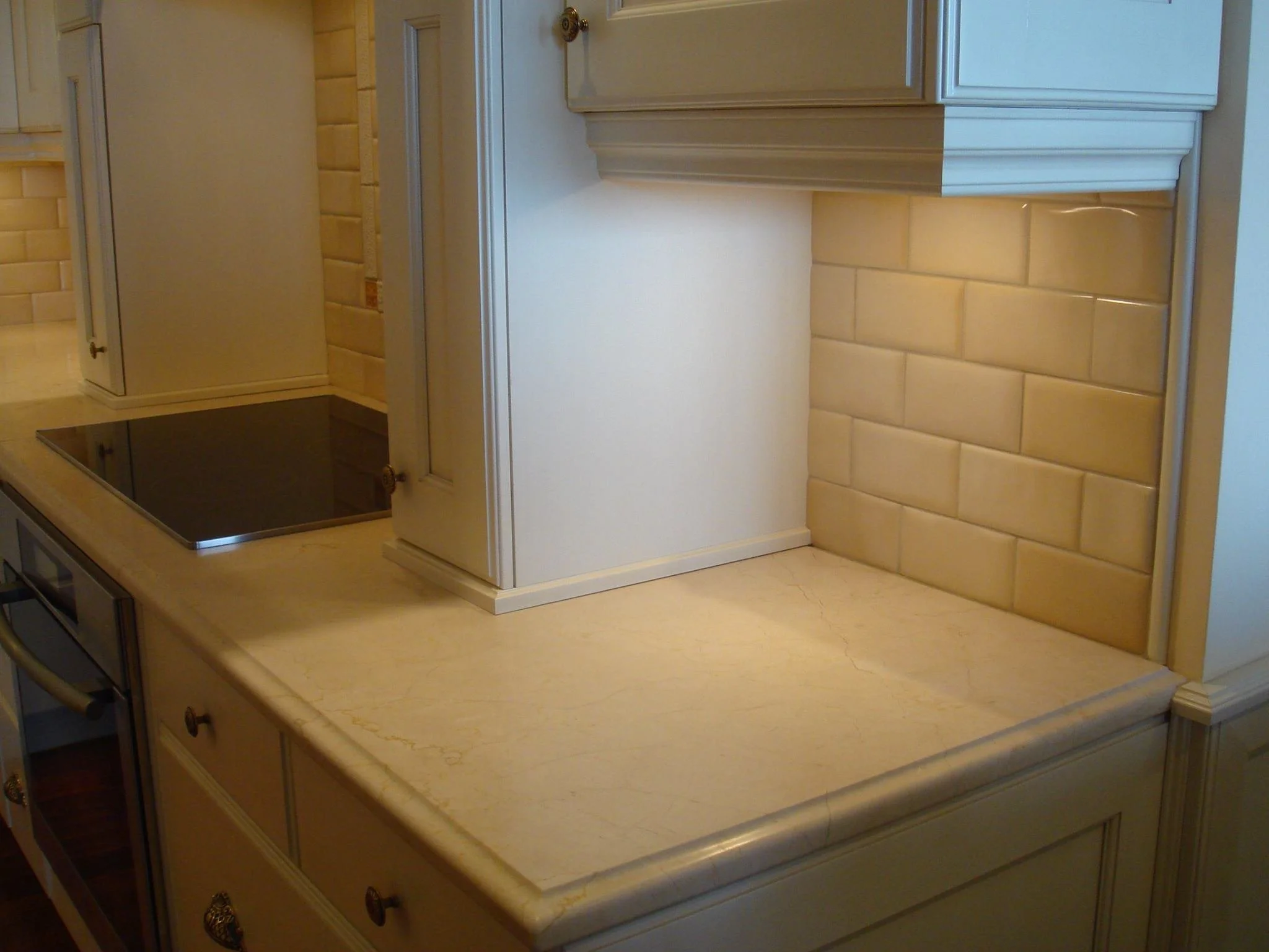 Kitchen countertop with beige marble surface, beige brick backsplash, and white cabinetry.