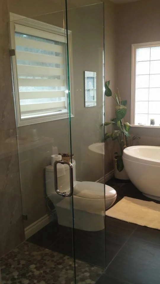 Bathroom with glass shower door, toilet, large freestanding bathtub, window, and potted plant.