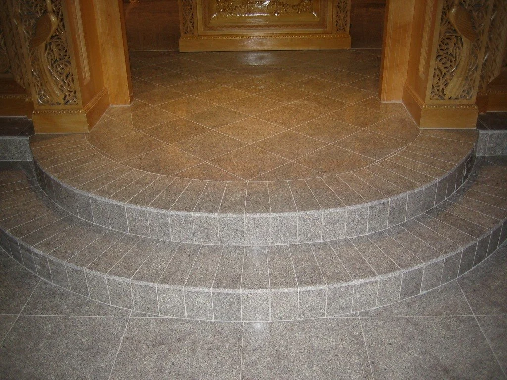 A staircase with gray tiles leading up to a decorated wooden platform or altar with intricate carvings.