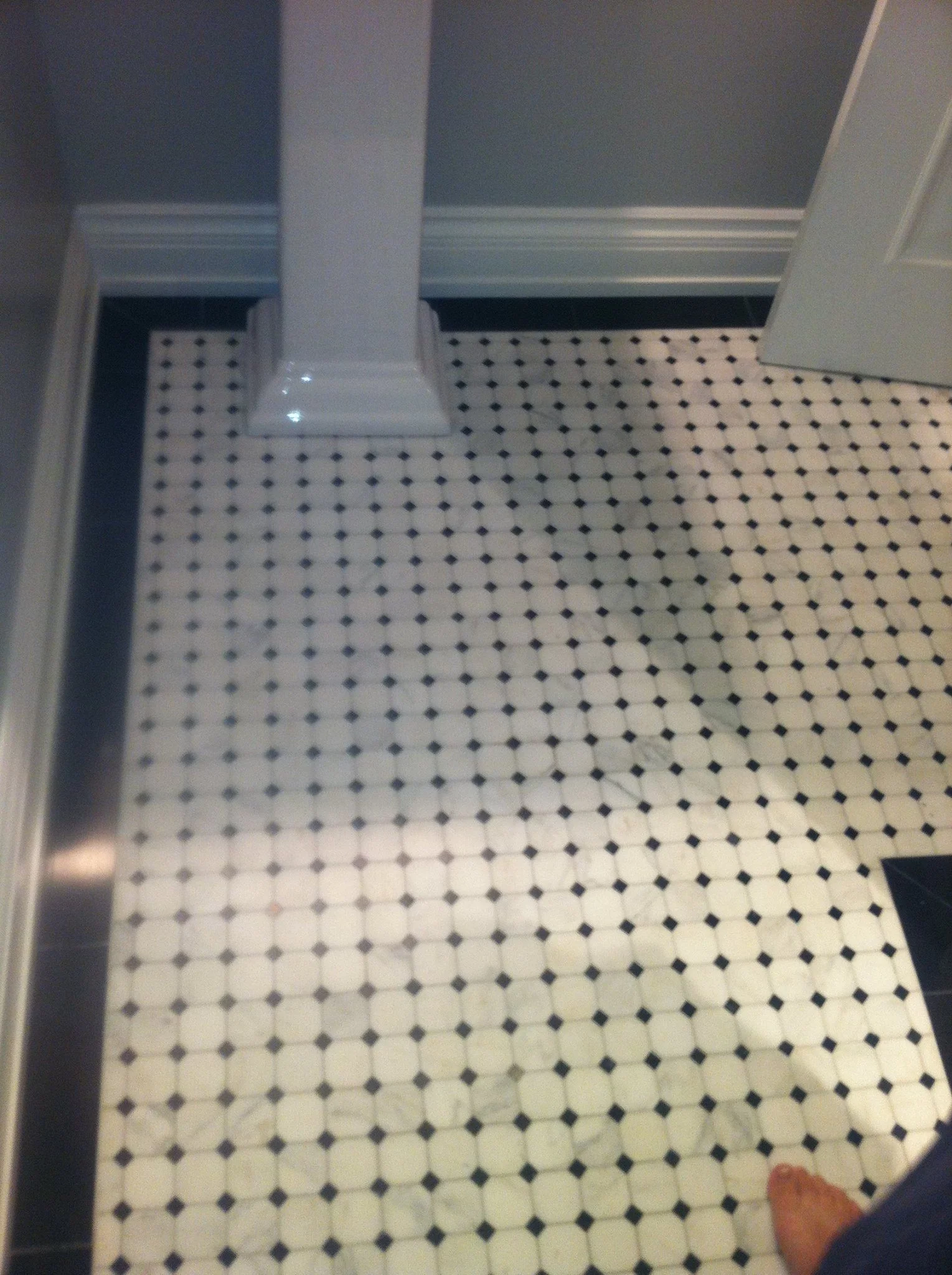Bathroom floor with black and white hexagon tiles, part of a white vanity, a gray wall, and a slightly open white door.