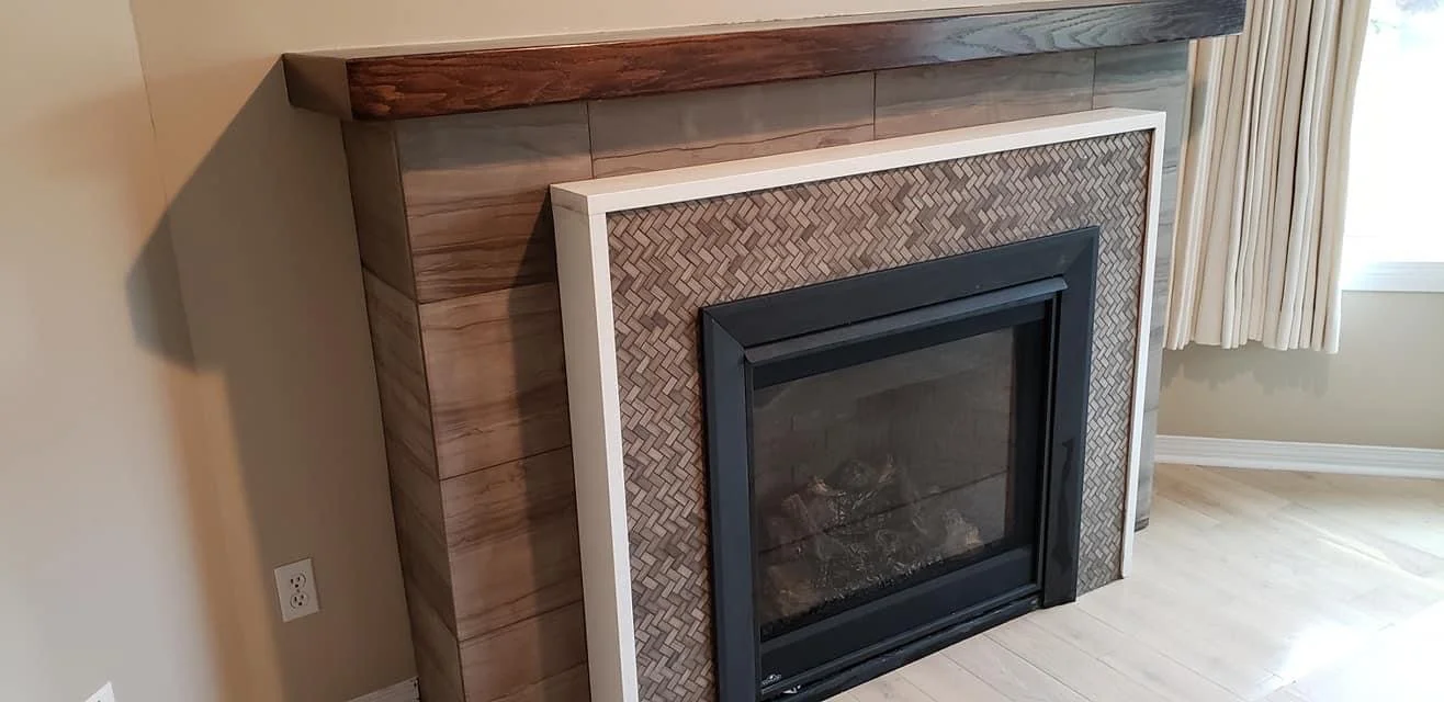 Wood-paneled fireplace with a decorative surround and a glass door, located next to beige walls, an electrical outlet, and a window with cream-colored curtains.