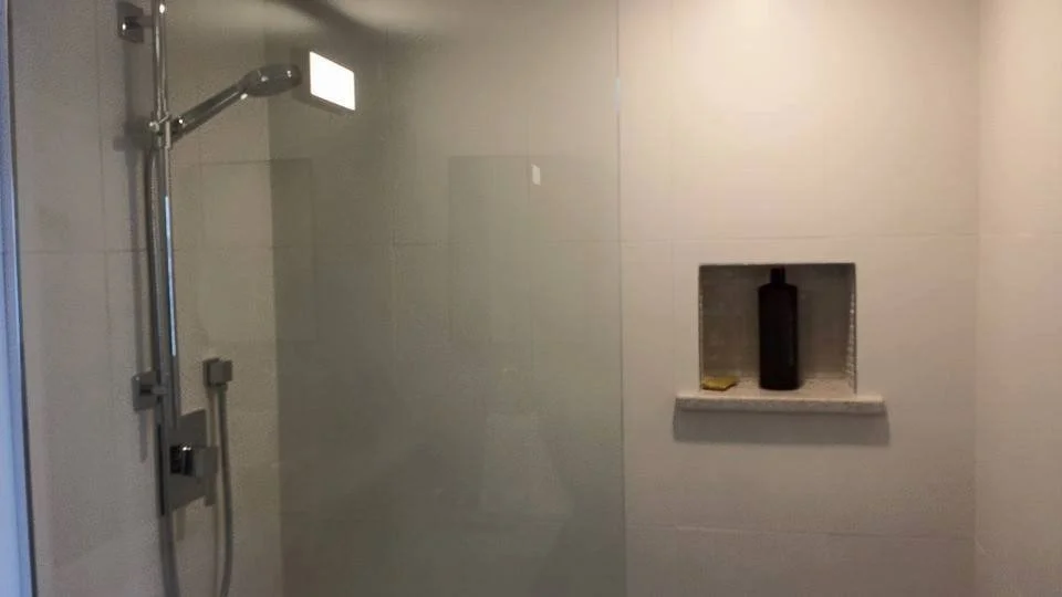 Shower area with a handheld showerhead and a built-in shelf holding a black bottle and a small item.