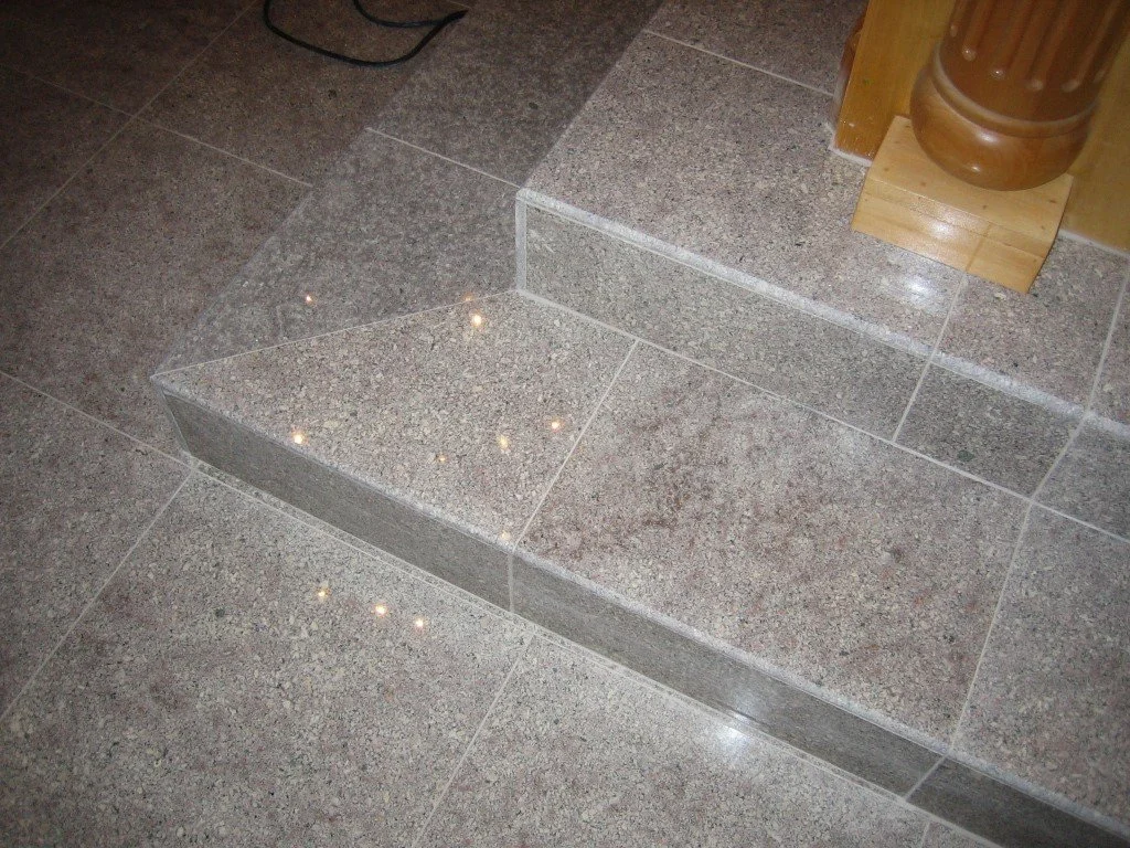 Close-up of granite tiled stairs with a small wooden fixture and a wooden object on top.