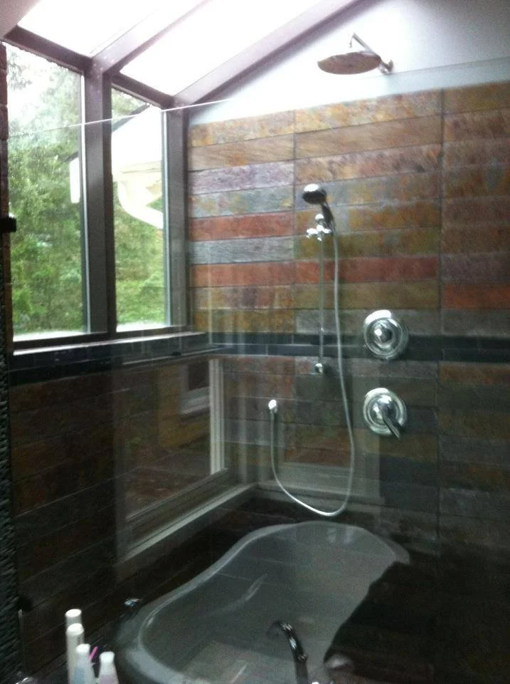 Bathroom with a bathtub, large window, and stone tile walls, natural light coming through the window.
