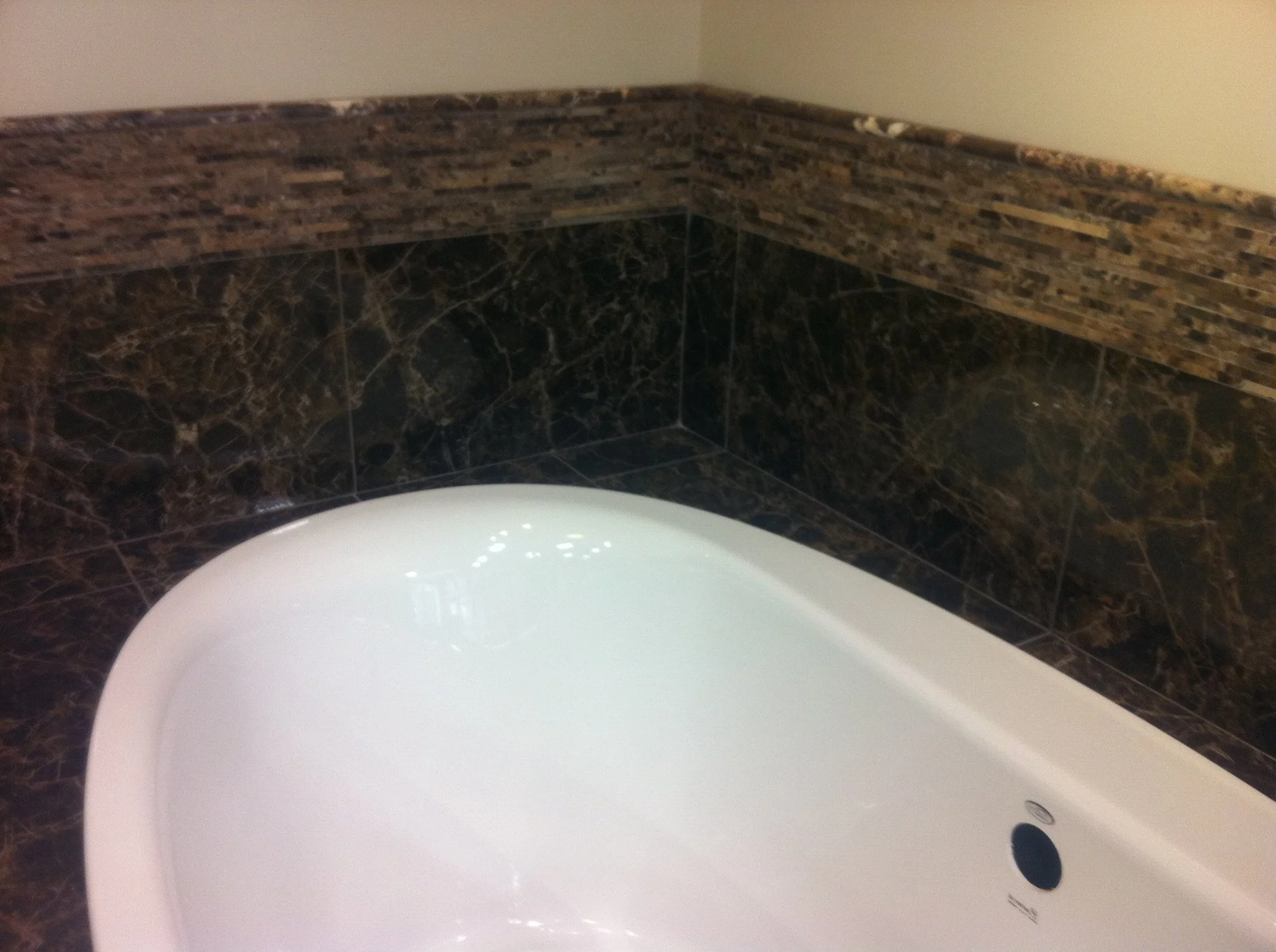Corner of a bathroom with dark marble tiles on the walls and a white bathtub.