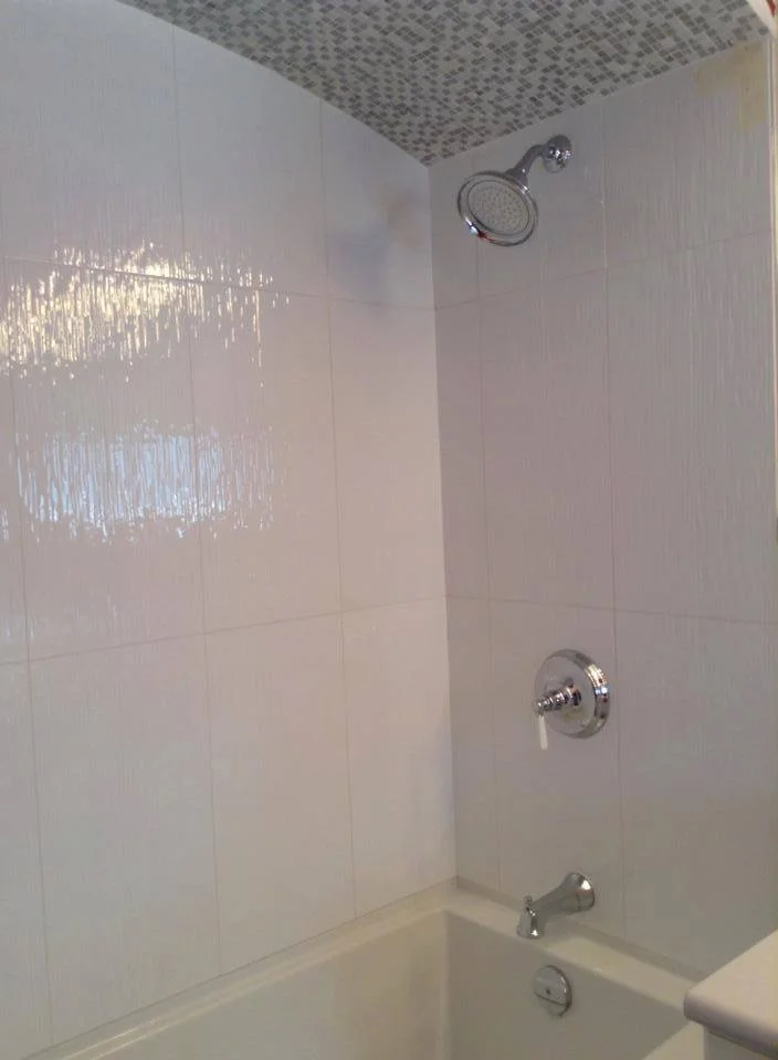 Bathroom shower with a round overhead showerhead, a single-handle valve, and a bathtub.