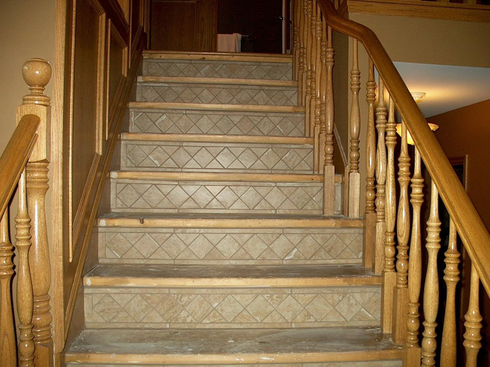 Wood staircase with beige and brown tiled steps, wooden handrails, and spindles in a home interior.