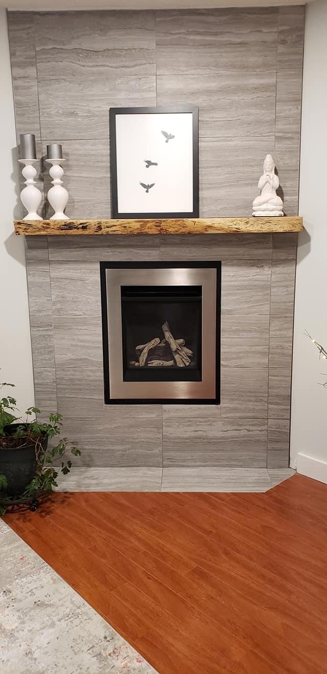 Living room fireplace with a wooden mantel, framed bird artwork above, decorative vases on the left, a Buddha statue on the right, and a potted plant on the left side of the fireplace.