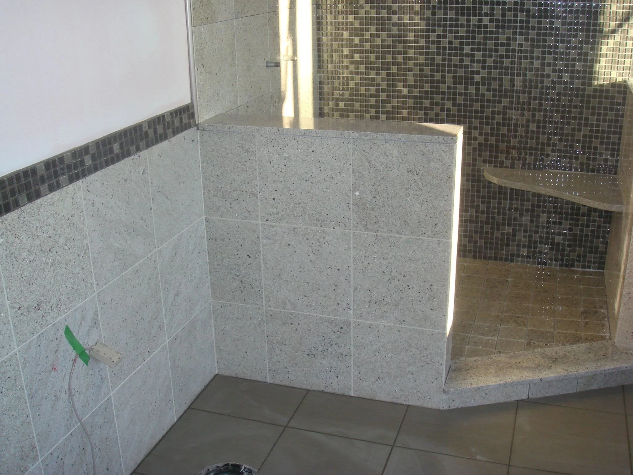 Indoor shower area with tiled walls and floor, featuring a corner with glass blocks and a shower head.