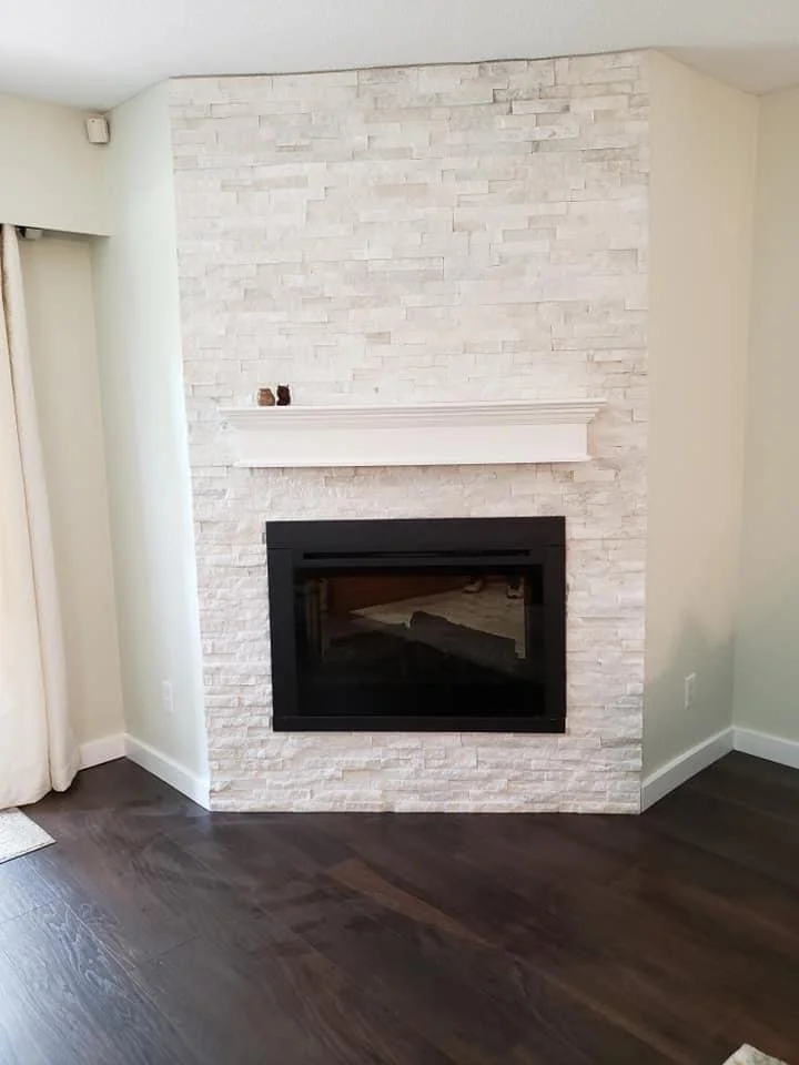 Interior of a room with a white stone fireplace, a white mantel, and dark wooden floors.