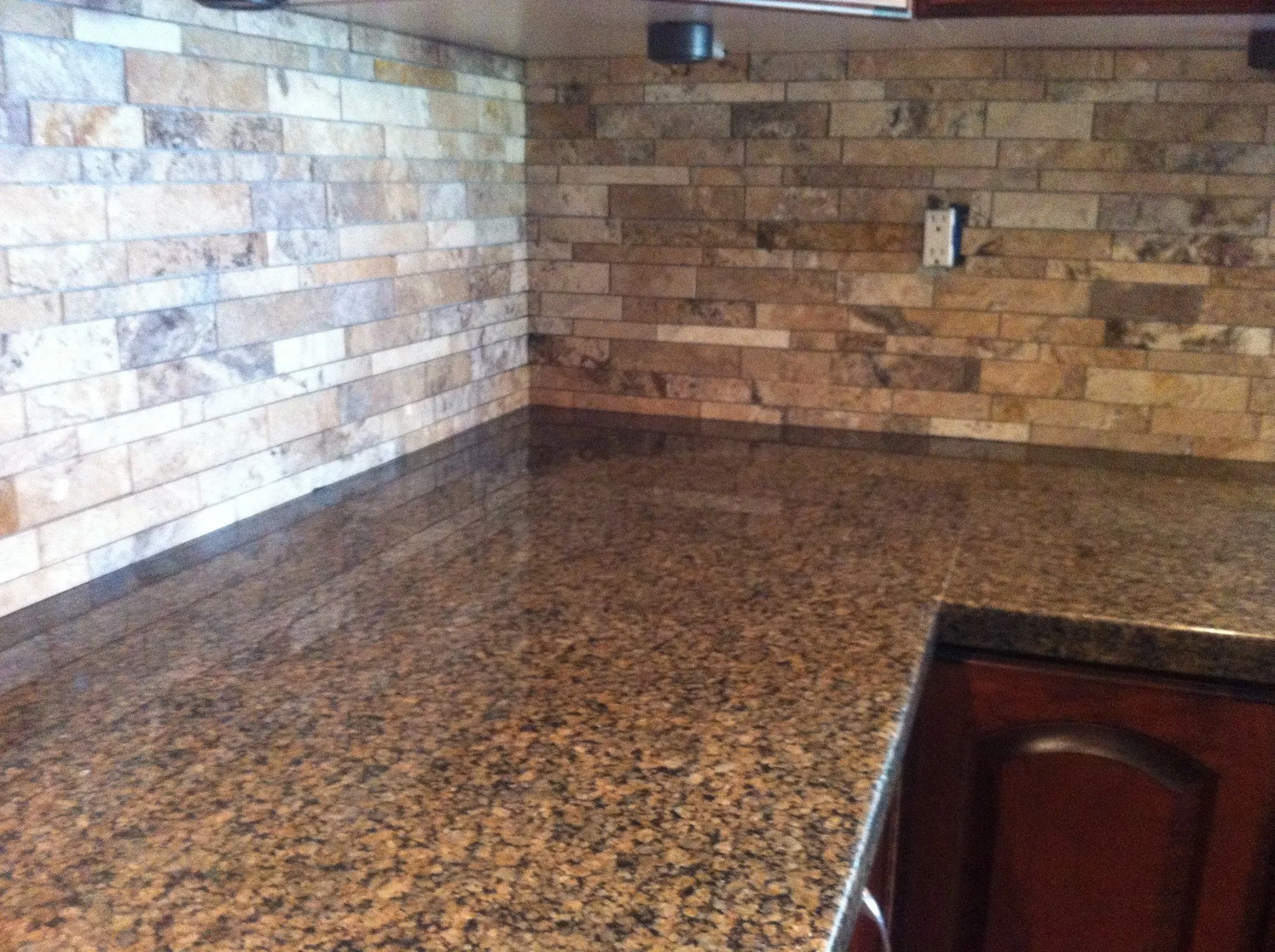 Close-up of a kitchen countertop with a speckled brown granite surface and brick backsplash wall.