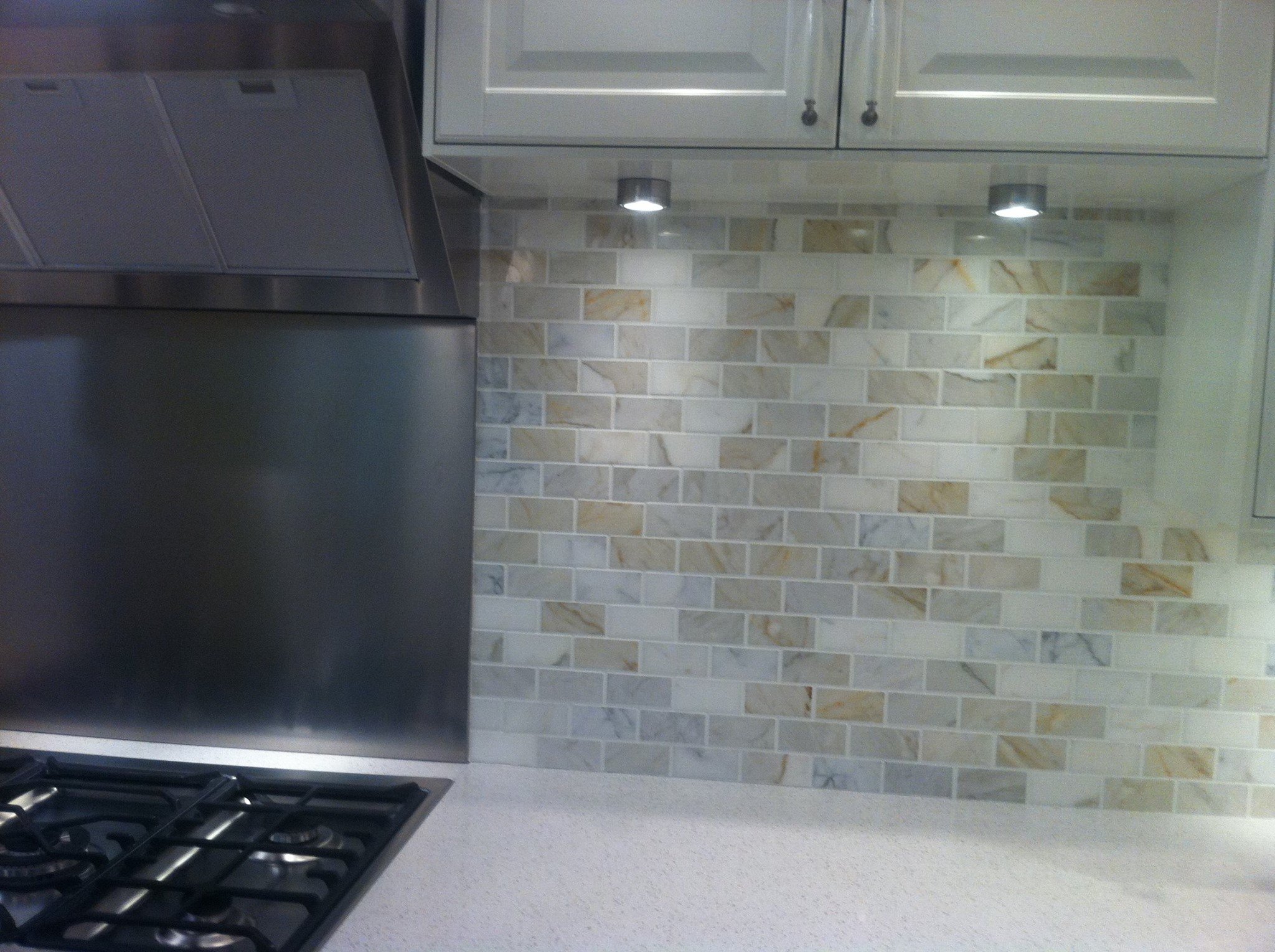 Kitchen with beige and white tiled backsplash, gray cabinets, and stainless steel appliances, including a range hood and a stove.