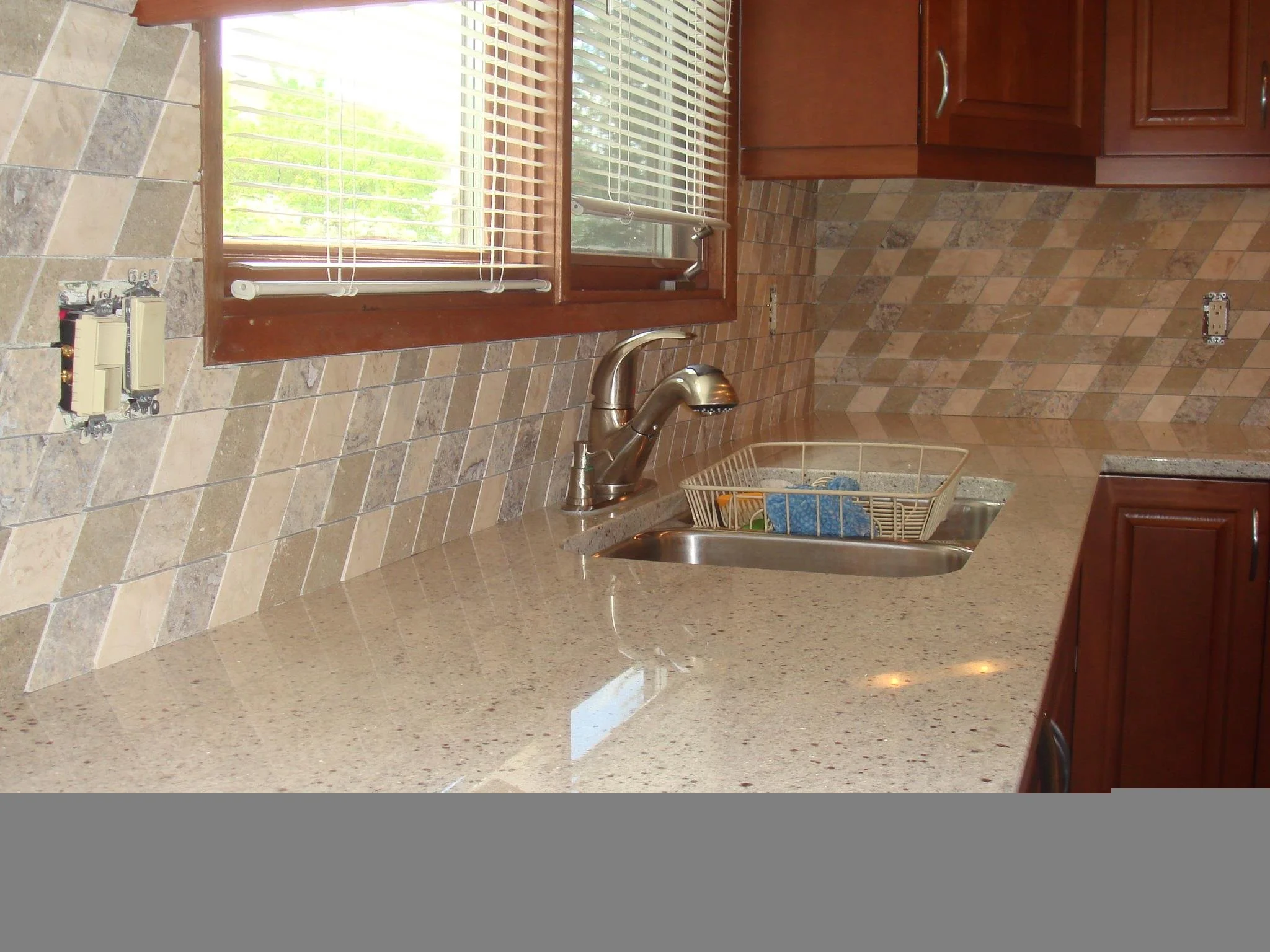 Kitchen countertop with a sink, window with blinds, and tile backsplash with a diamond pattern.