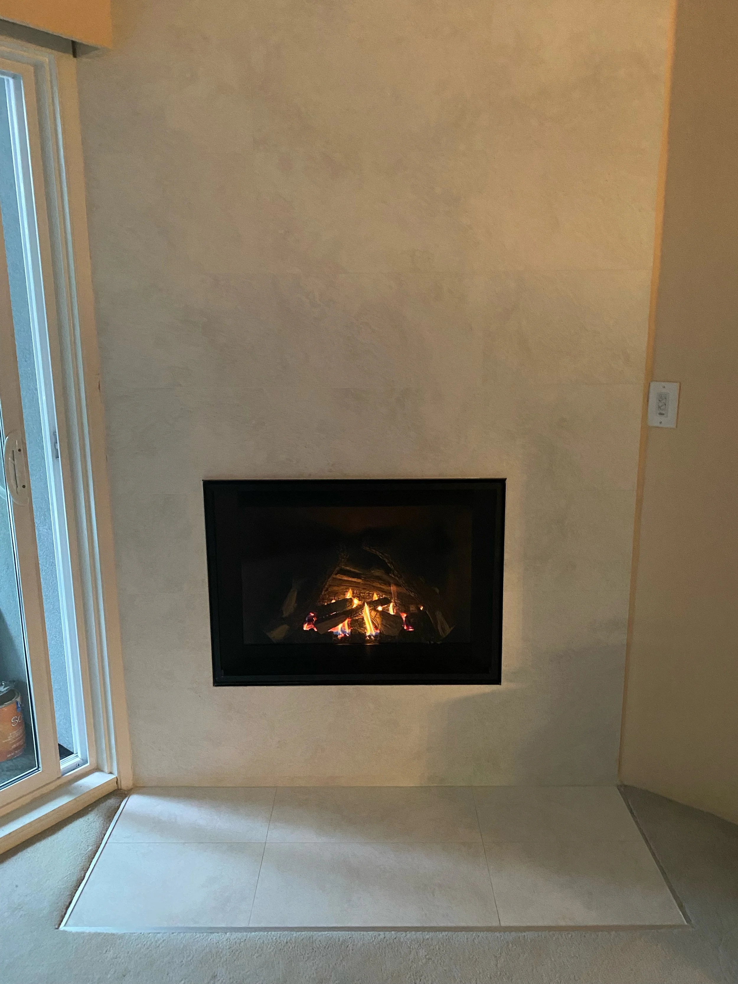 Modern fireplace with a fire burning inside, set into a beige wall in a living room.