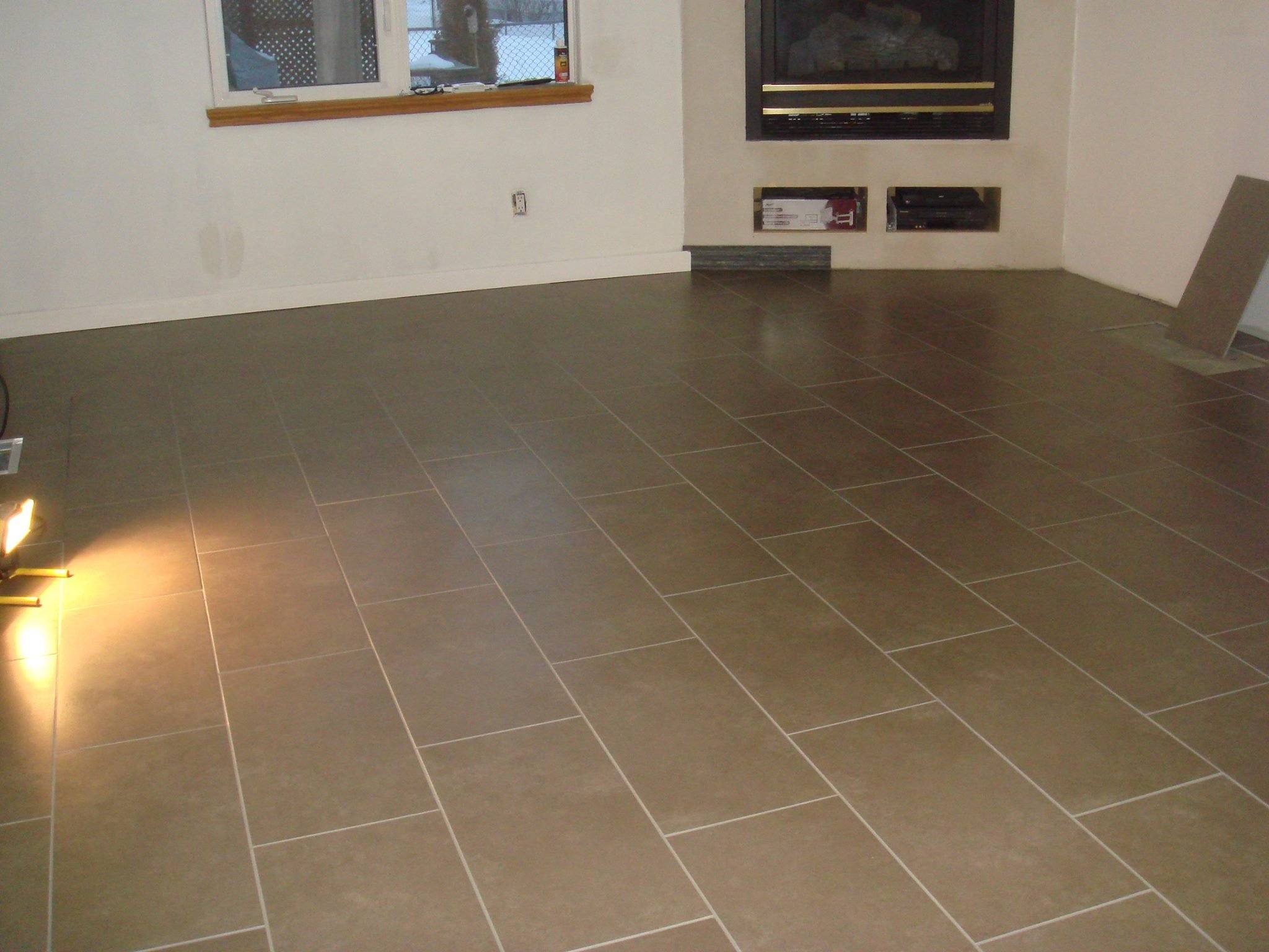 Empty living room with brown tiled floor, white walls, a window, and a fireplace