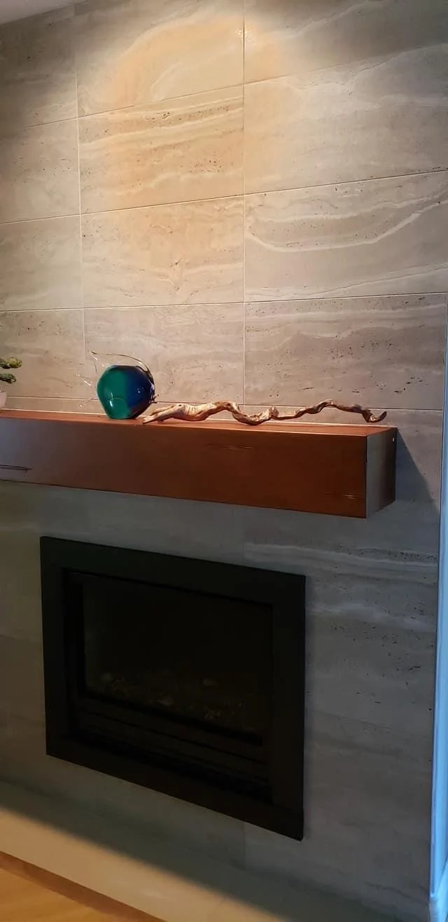 Decorative shelf with a glass bowl and a piece of driftwood above a fireplace in a living room with beige marble wall tiles.