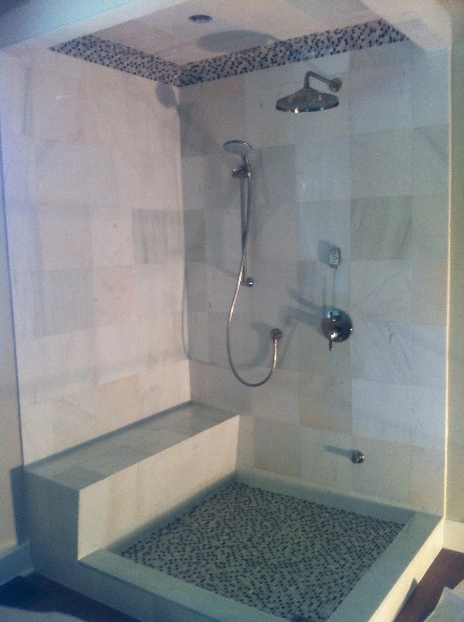 A modern walk-in shower with a rain shower head, a handheld shower, and a built-in bench, with tiled walls and a pebble tile floor.