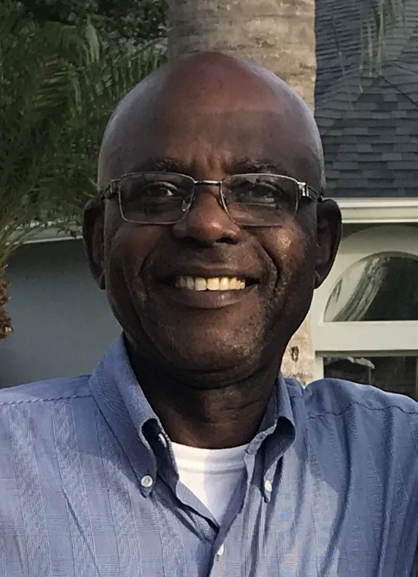 Sebastian Ekwotafia wears a blue button up and glasses and smiles at the camera.