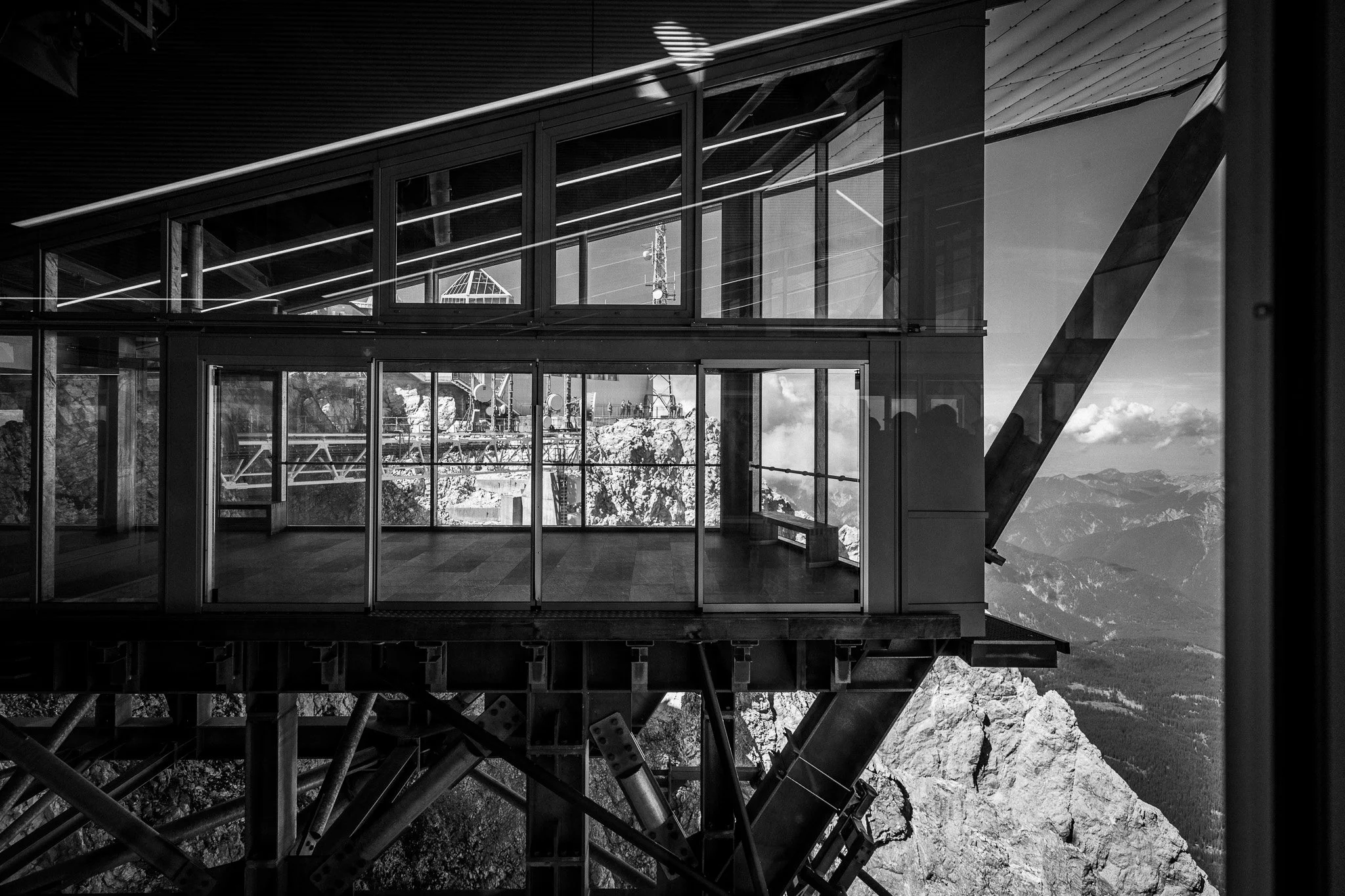 Moderne Aussichtsplattform mit Glaswänden, gebaut in den Bergen, bei sonnigem Himmel, schwarz-weiß Fotografie.