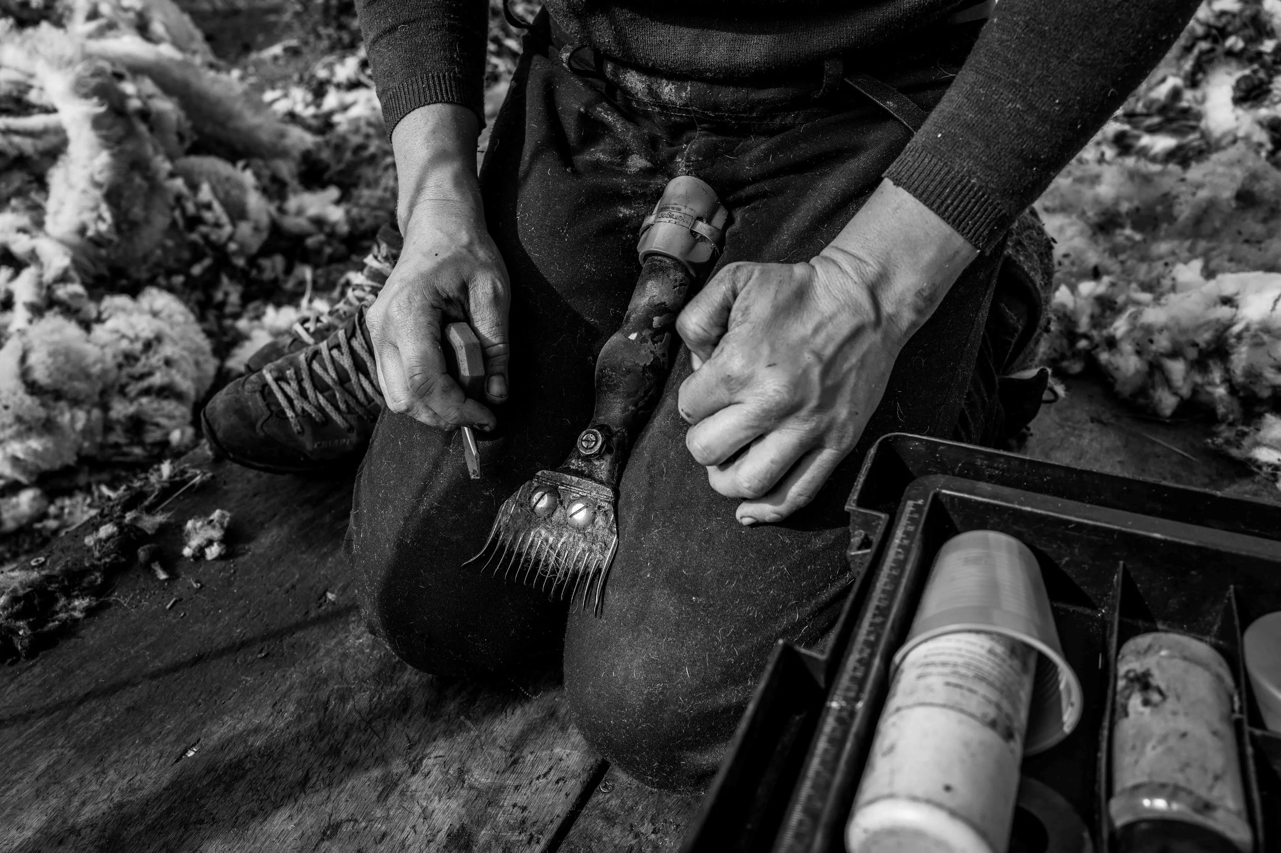 Mensch sitzt im Freien auf einem Holzblock und arbeitet mit Gartenwerkzeugen, darunter ein Holzhaken, mit Gartenarbeit im Schnee.