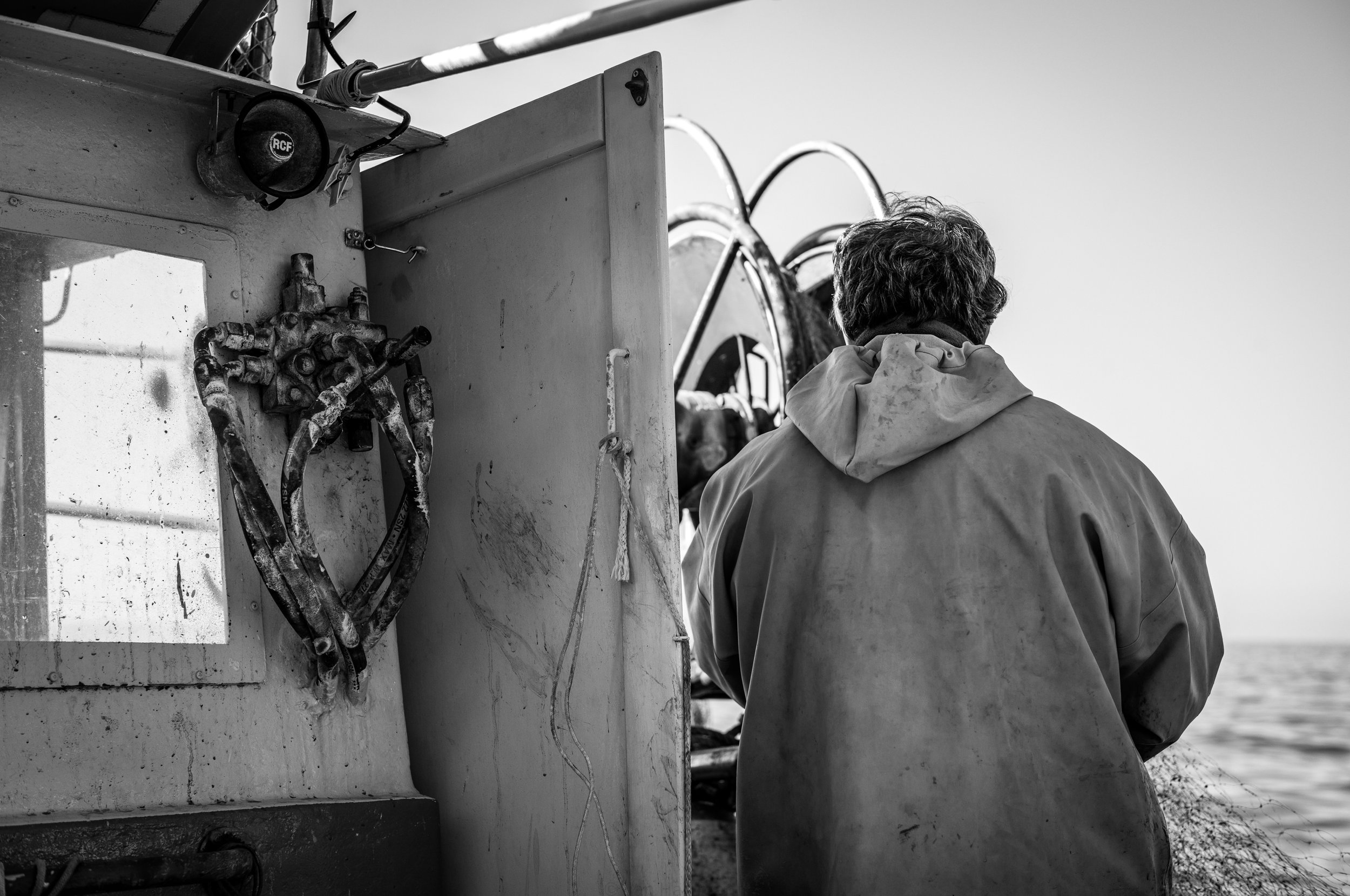 Ein Mann steht auf einem Boot, blickt aufs Meer, im Hintergrund ist das Wasser zu sehen, in schwarz-weiß.