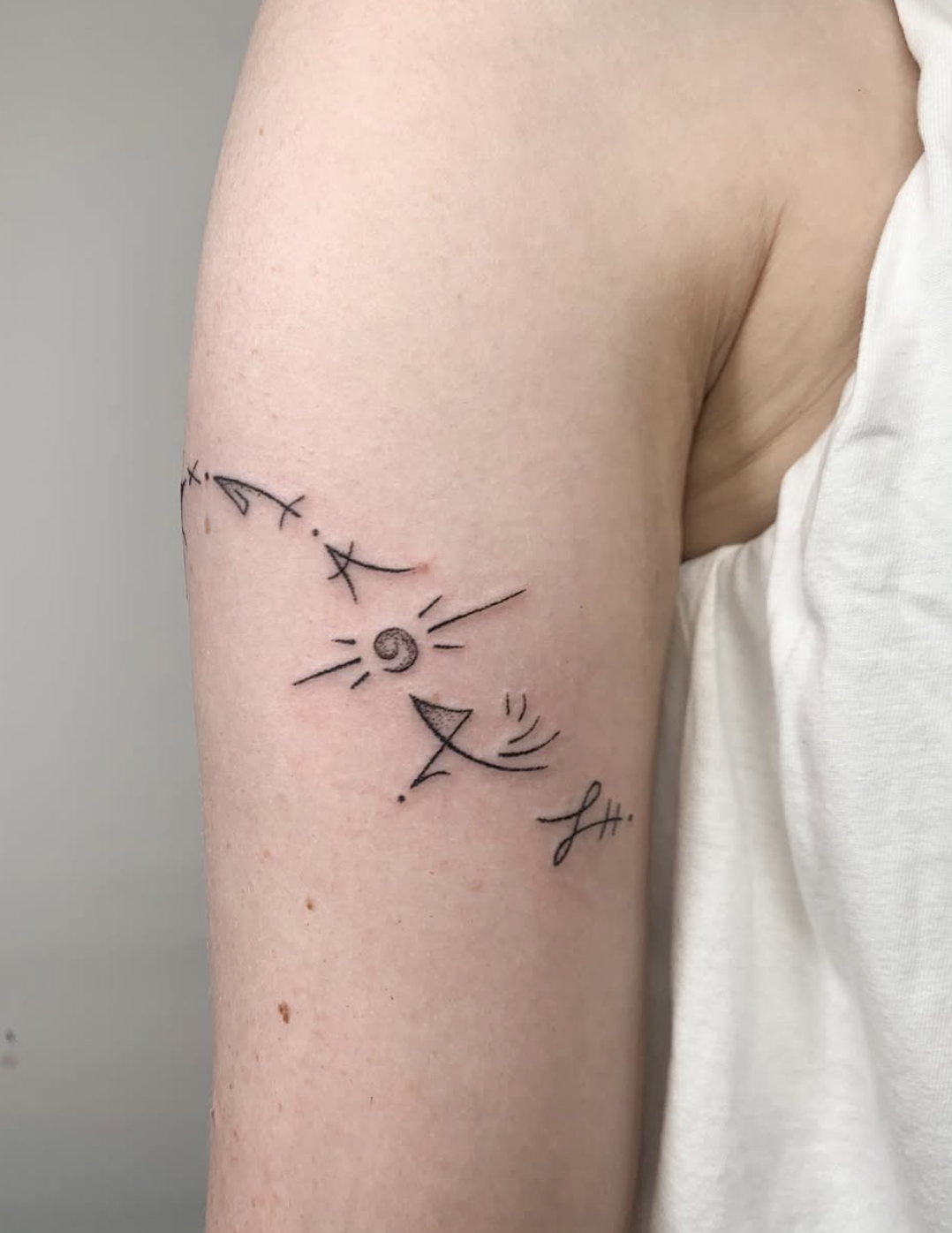 Tattoo on the upper arm featuring a sun, moon, star, shooting star, and abstract lines.