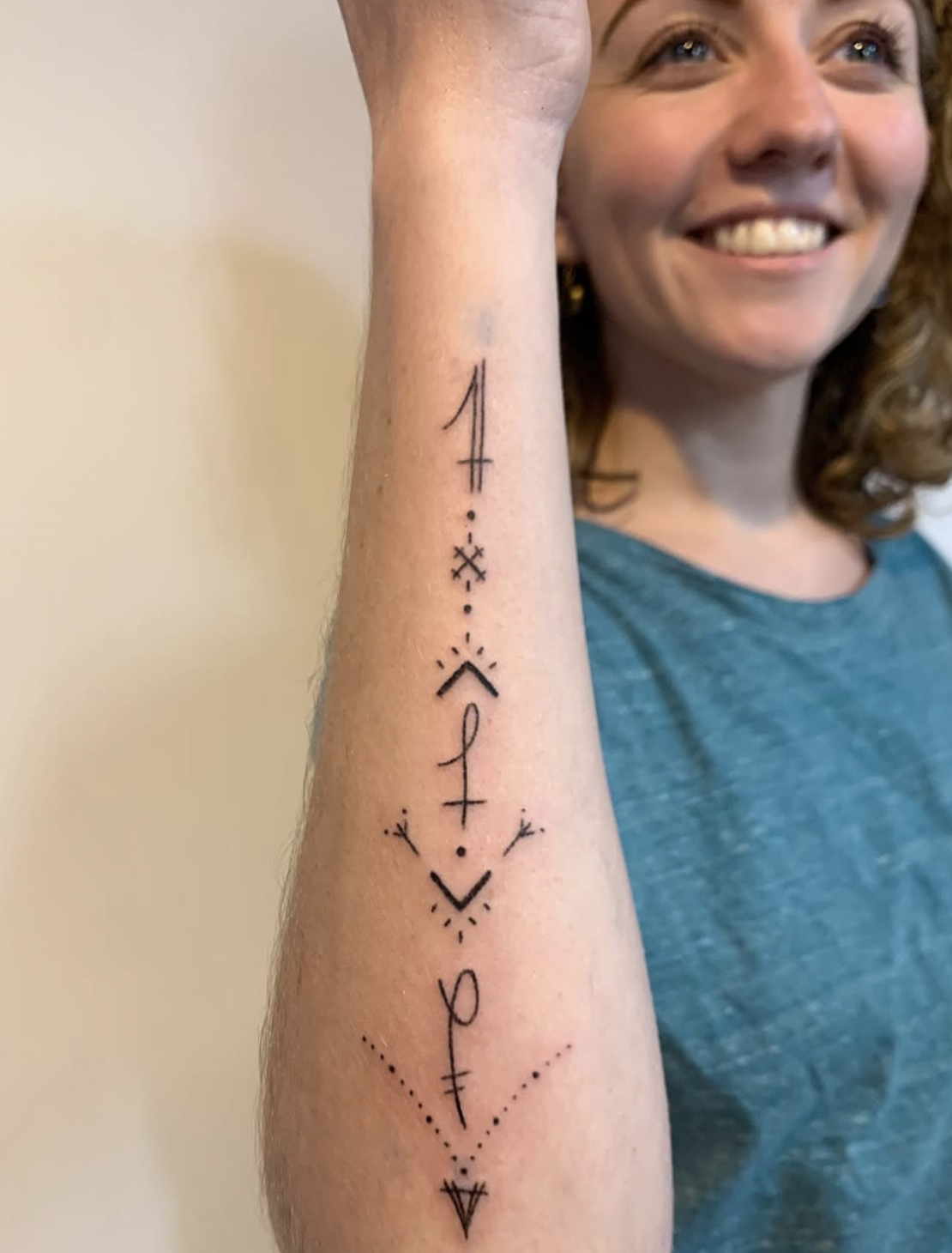 Tattoo on woman's forearm featuring geometric symbols, lines, dots, and arrow motifs arranged vertically.