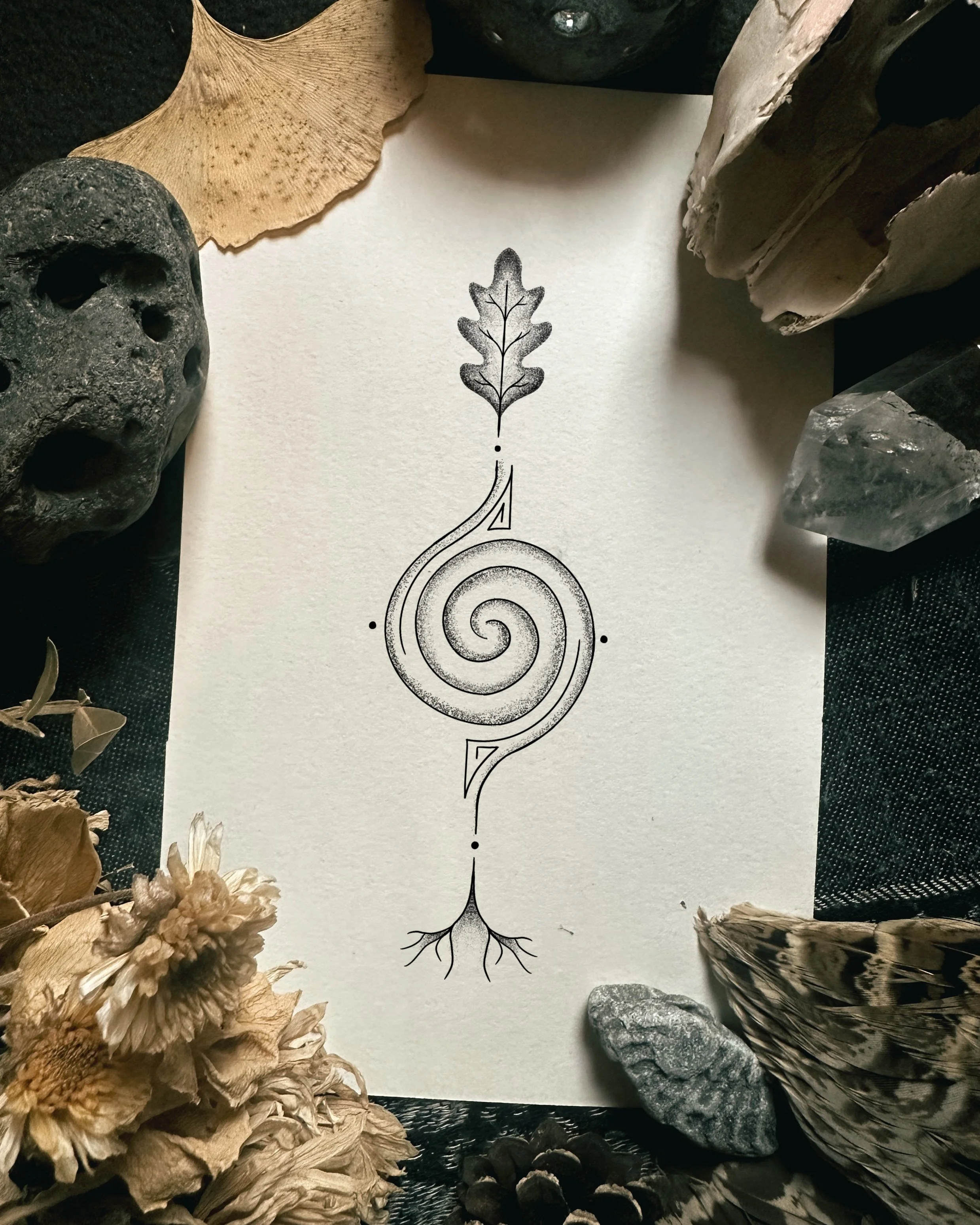 Black and white sketch of an oak leaf with decorative elements, surrounded by dried flowers, rocks, and wood pieces.