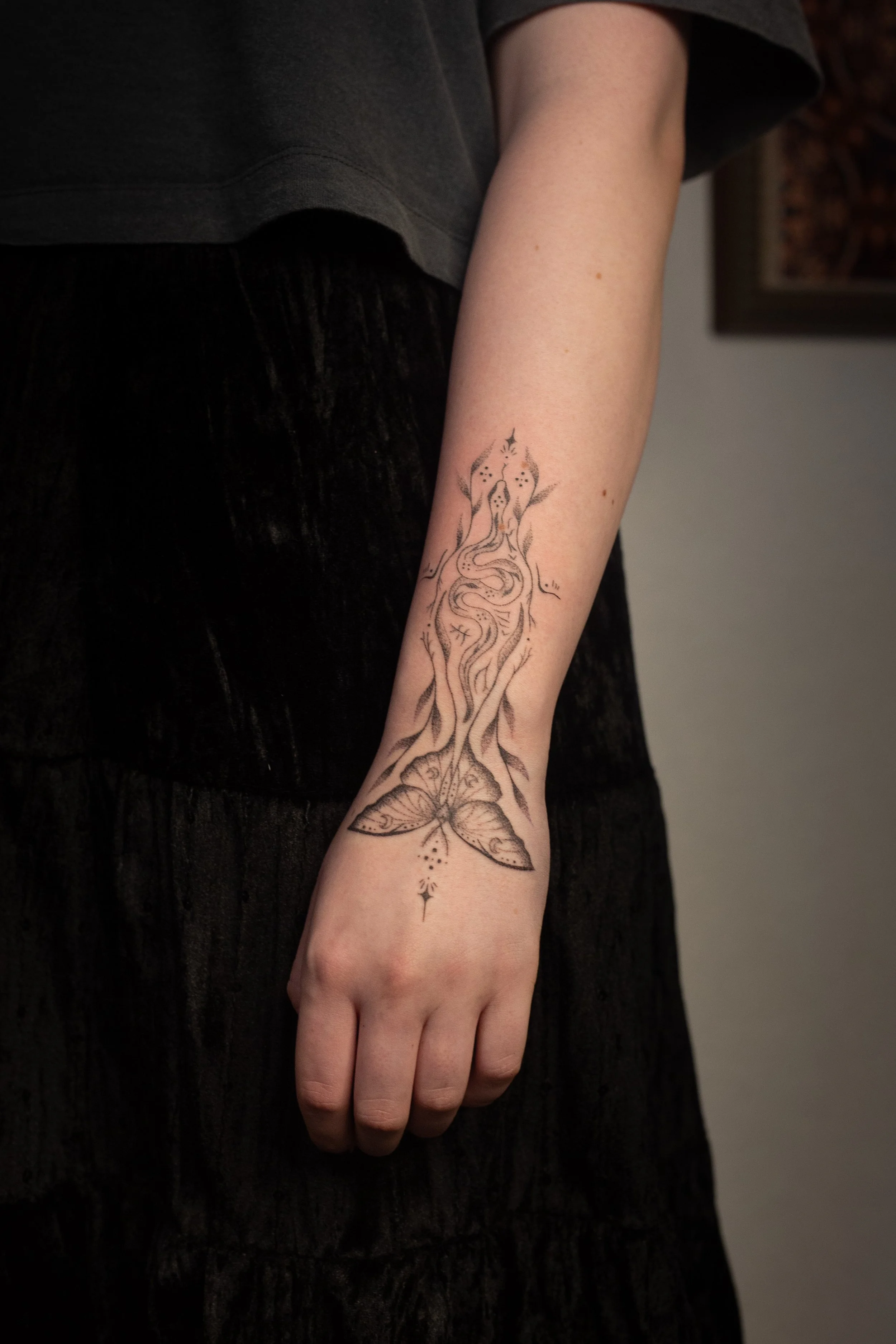 A person's arm with a detailed black ink butterfly and moth tattoo extending from the wrist to the forearm.