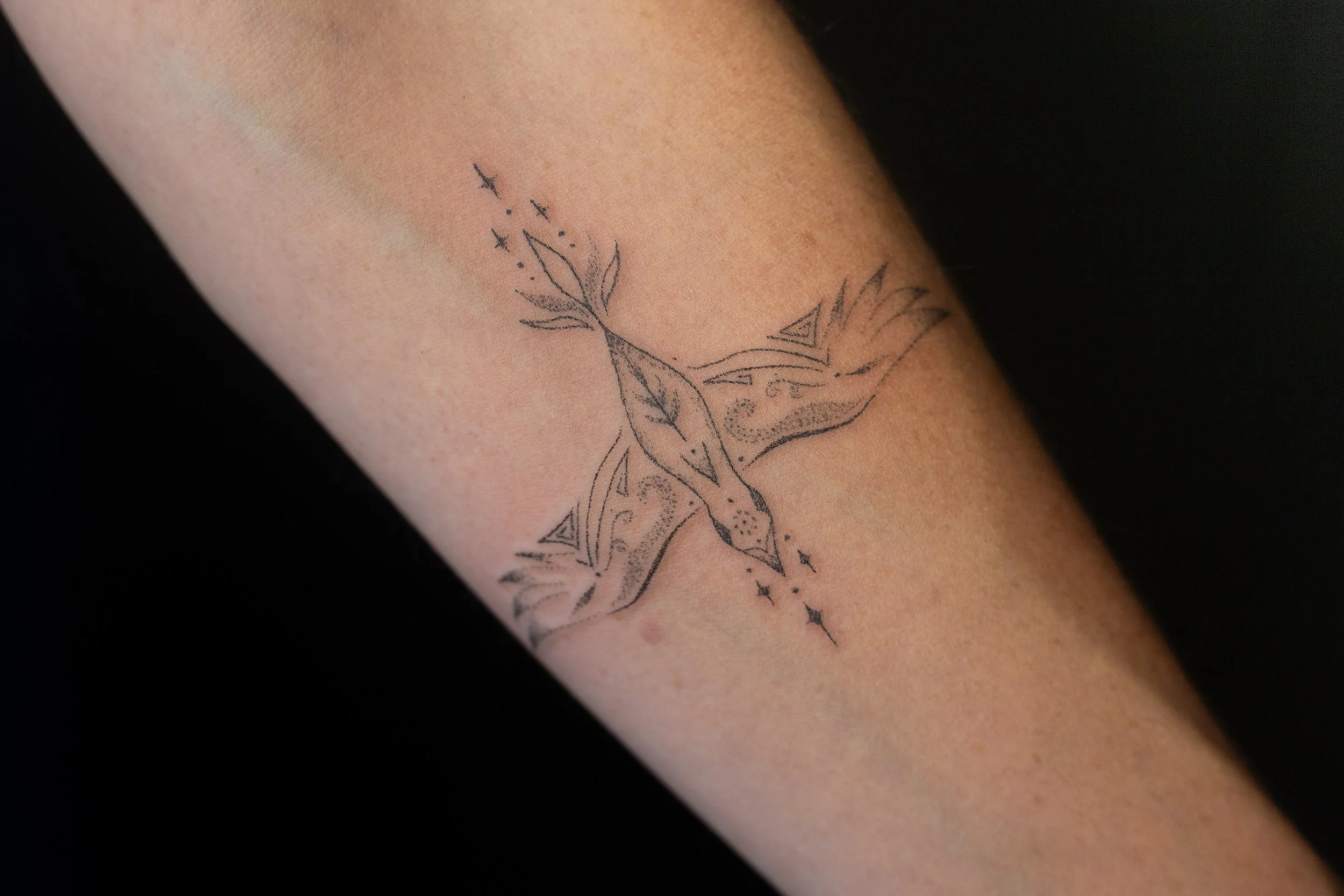 Close-up of a tattoo on a person's arm featuring a stylized deer head with antlers, surrounded by celestial elements like stars and a dotted line.
