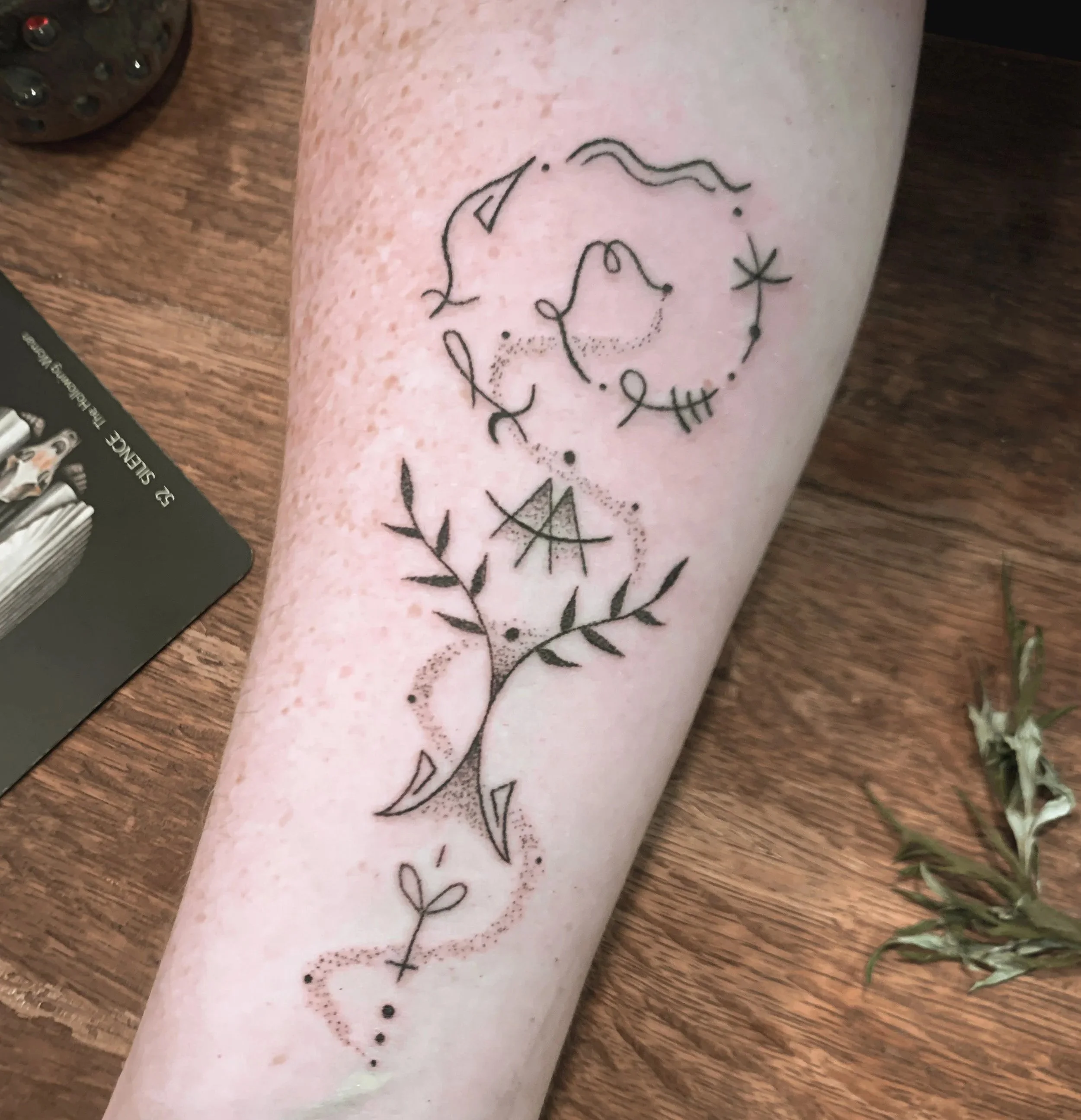 Tattoo of a couple's faces in profile, surrounded by a circle of stars, leaves, and decorative elements on a person's arm.