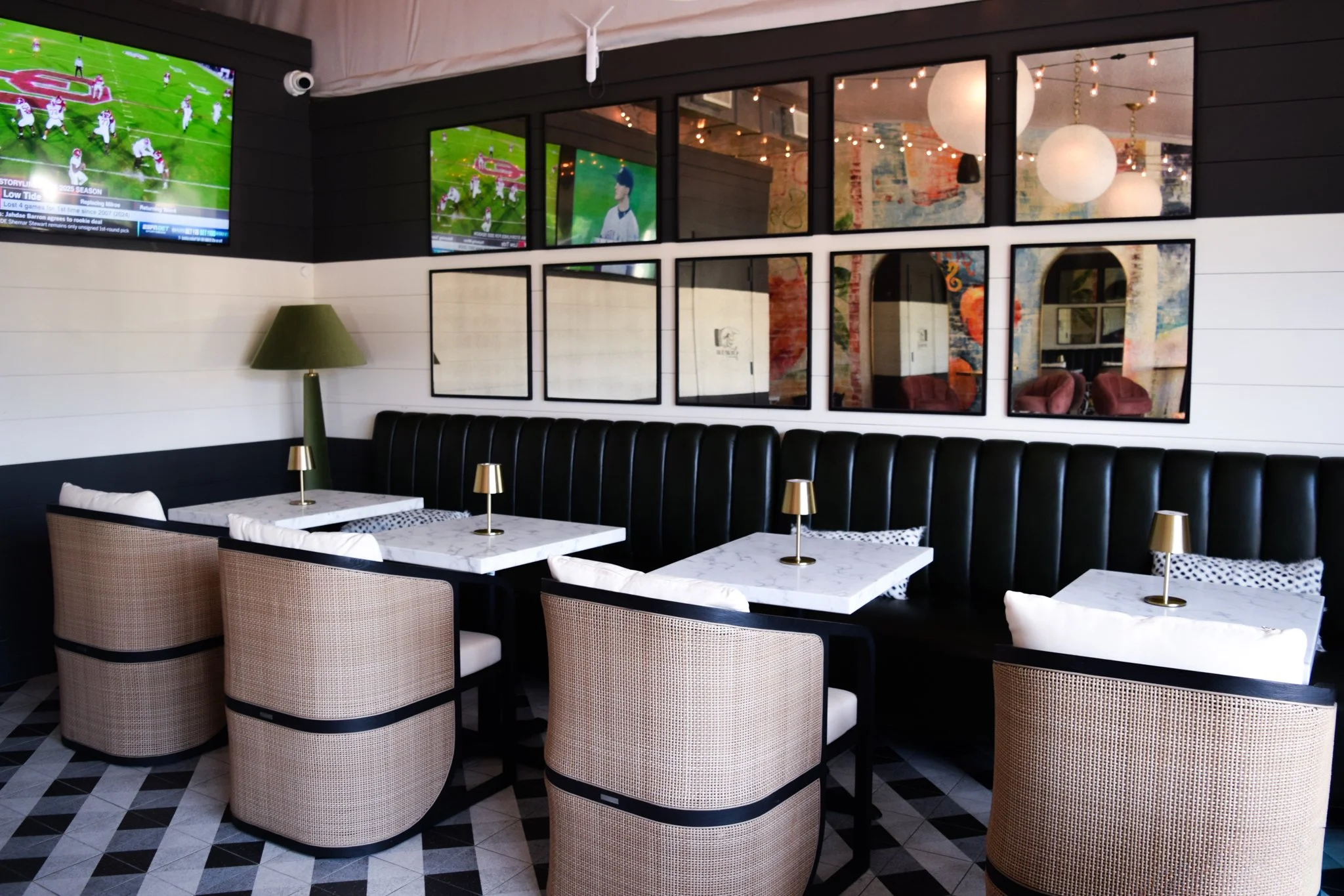 Modern restaurant interior with white marble tables, beige chairs, black leather booth seating, gold desk lamps, and black-framed mirrors on a dark wall.