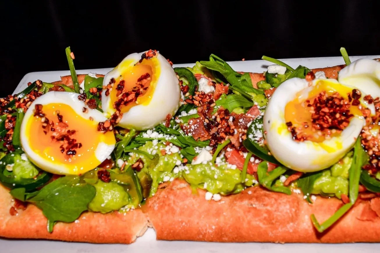 Open-faced sandwich with leafy greens, halved soft-boiled eggs topped with red pepper flakes, on a crusty bread slice