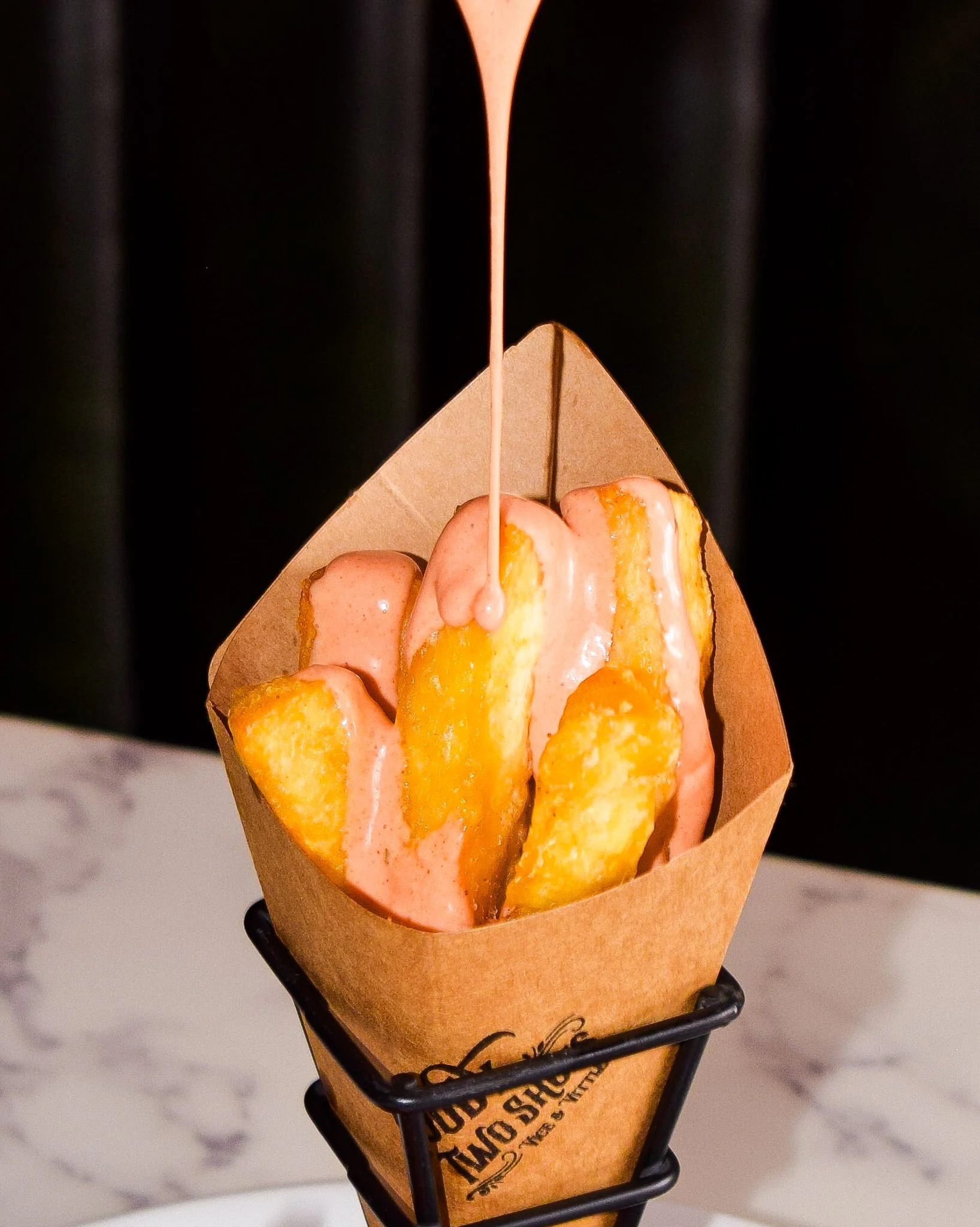 French fries topped with melted cheese and gravy, inside a paper cone in a metal holder.