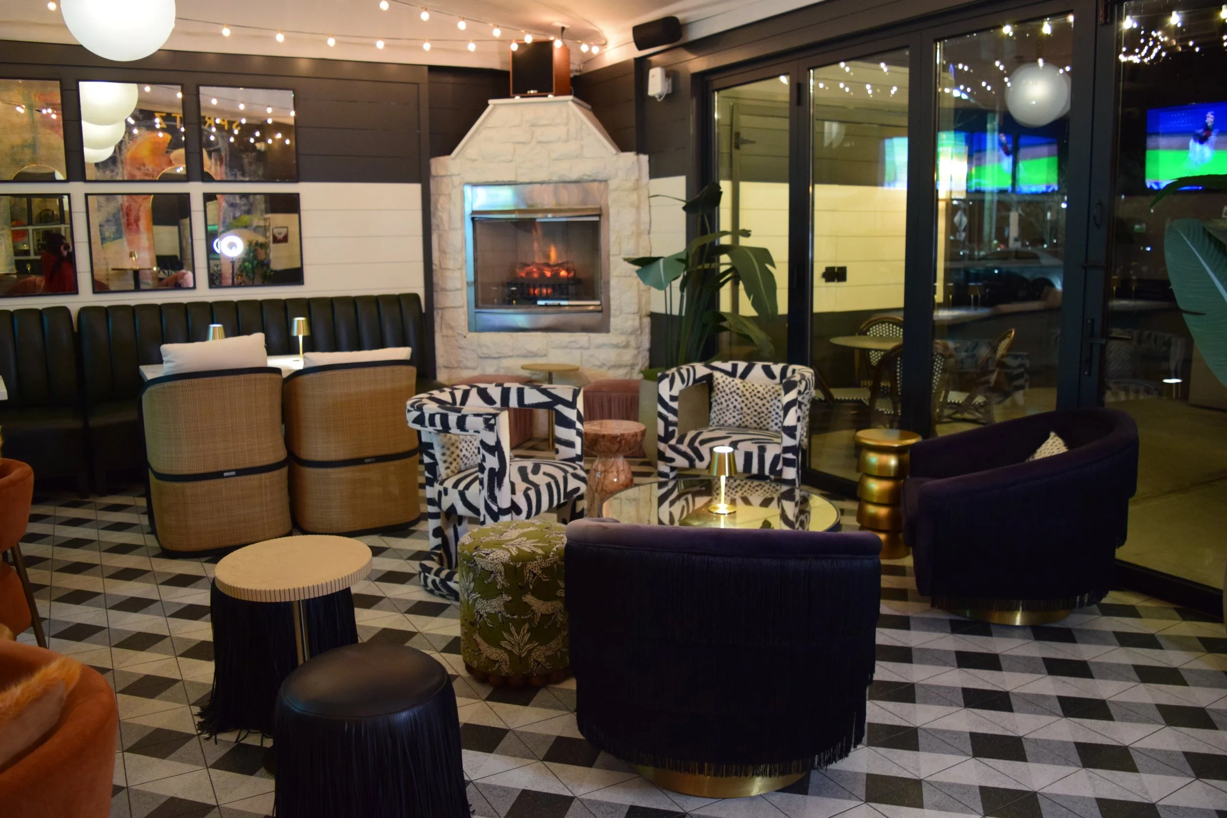 Interior of a modern lounge with a fireplace, patterned chairs, black velvet chairs, a small round table, and decorative lighting.