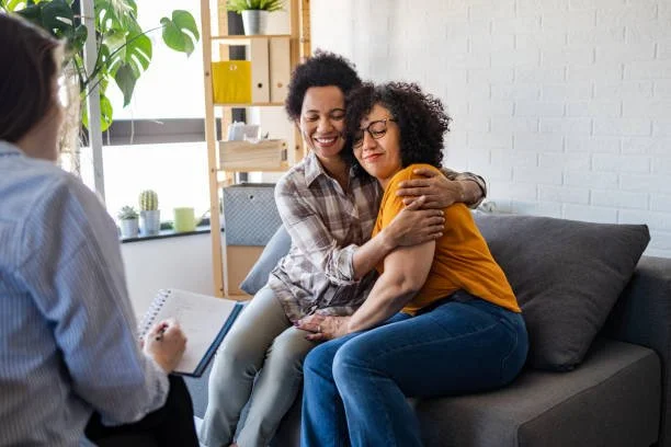 Two women hugging while talking to a therapist in a therapy session.