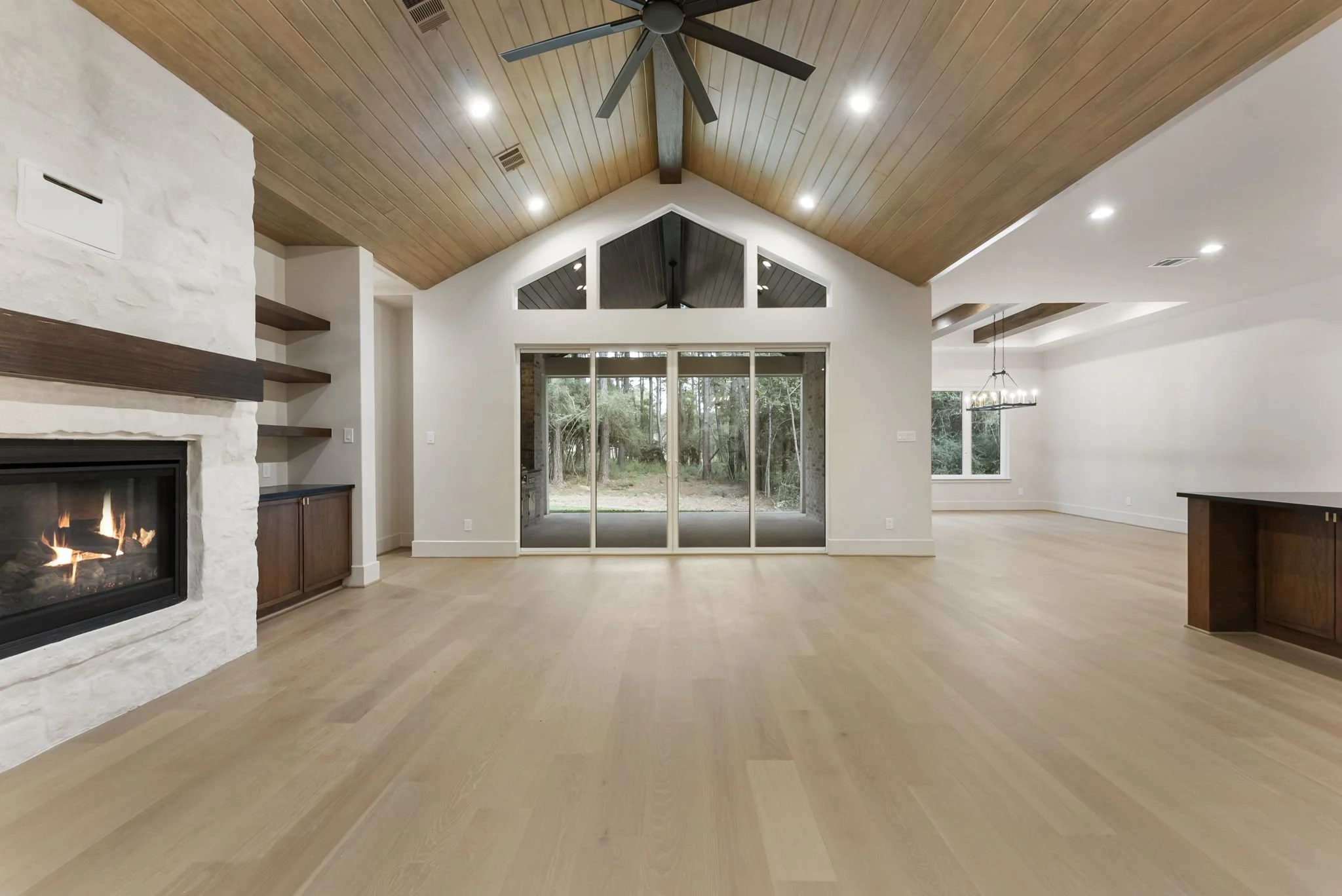 Empty living room with large glass sliding door, fireplace, wooden ceiling with ceiling fan, and hardwood flooring.